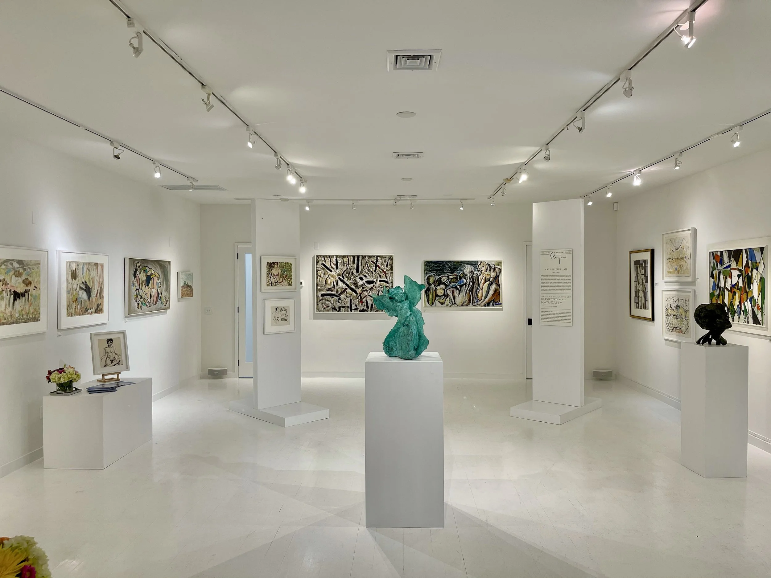 A modern art gallery with white walls and ceiling, featuring various abstract paintings and sculptures displayed on white pedestals.