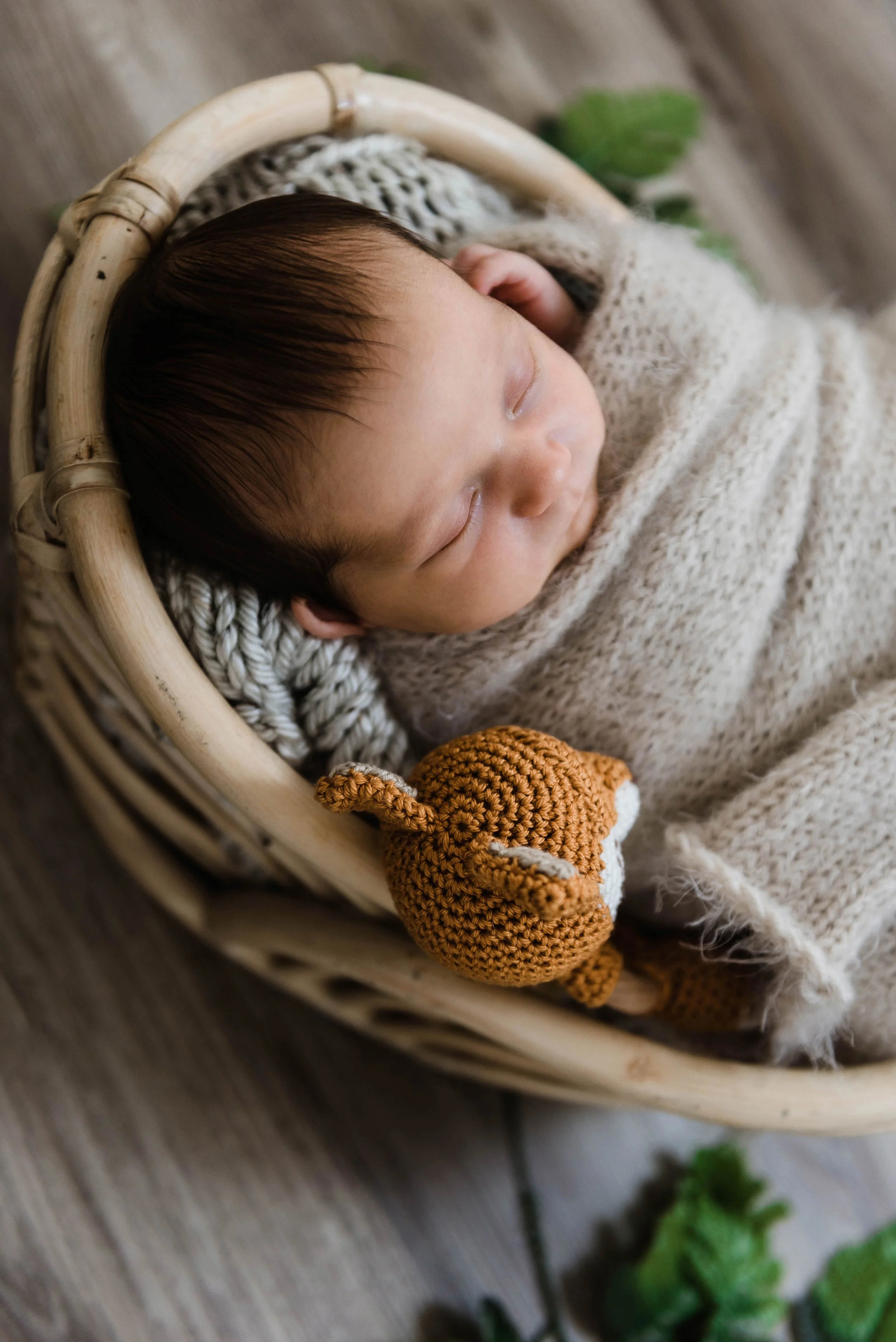 A sleeping baby wrapped in a cozy knitted blanket, lying in a woven basket with a small crocheted fox nearby. Studio newborn portrait, Brownsville PA.