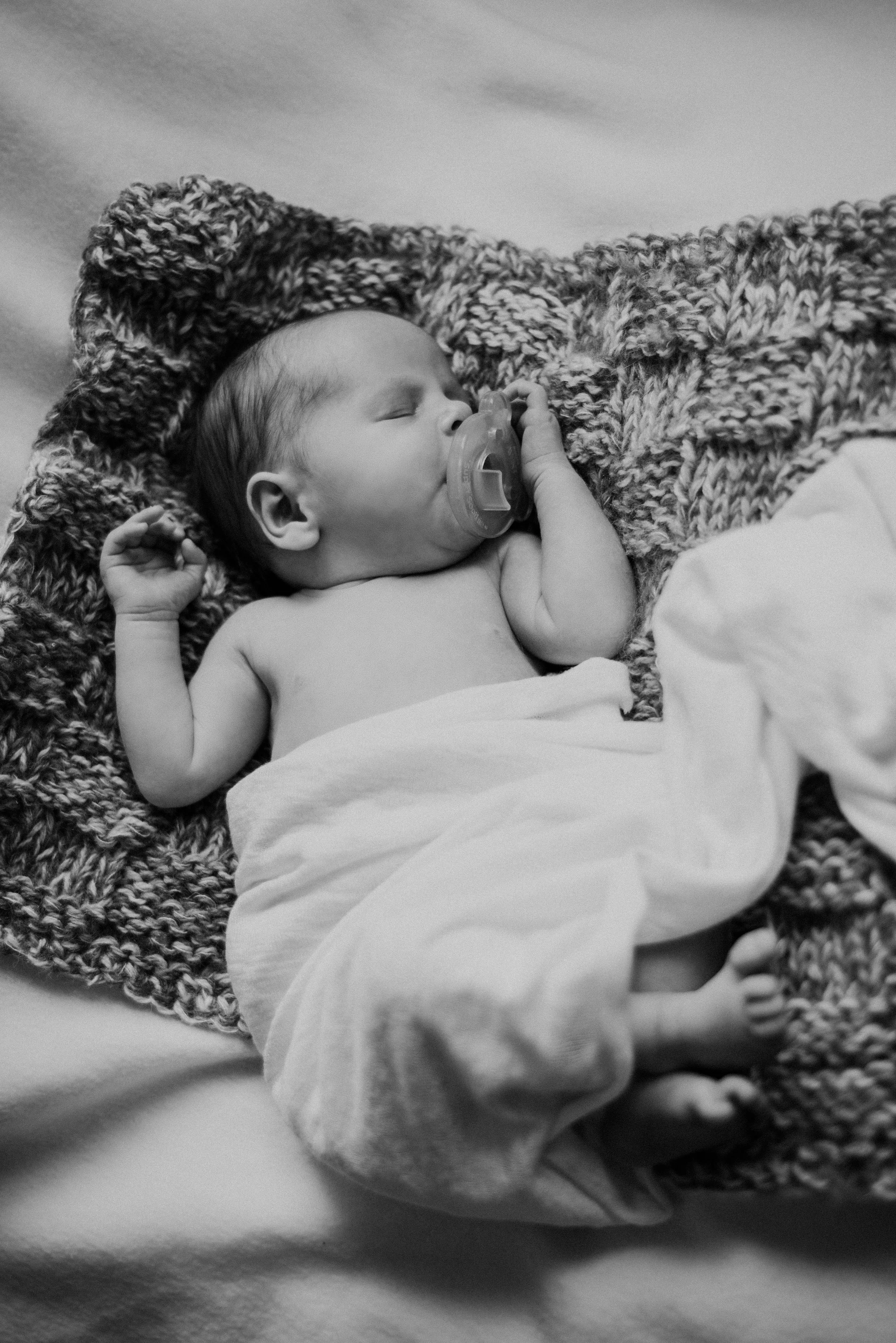 A sleeping baby lying on a knitted blanket with a pacifier in their mouth, wearing a cloth diaper. Studio newborn portrait, Brownsville PA.