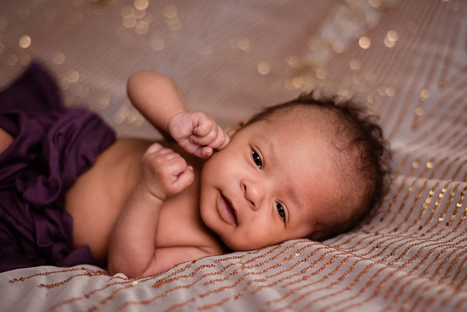 newborn is awake and happy, stretched out on pink and gold sequined fabric