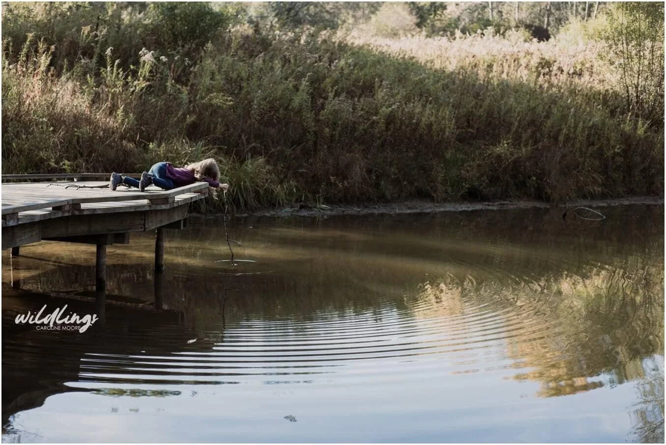 A toddler "goes fishing" with her stick in the lake at Beechwood Nature Reserve in Pittsburgh