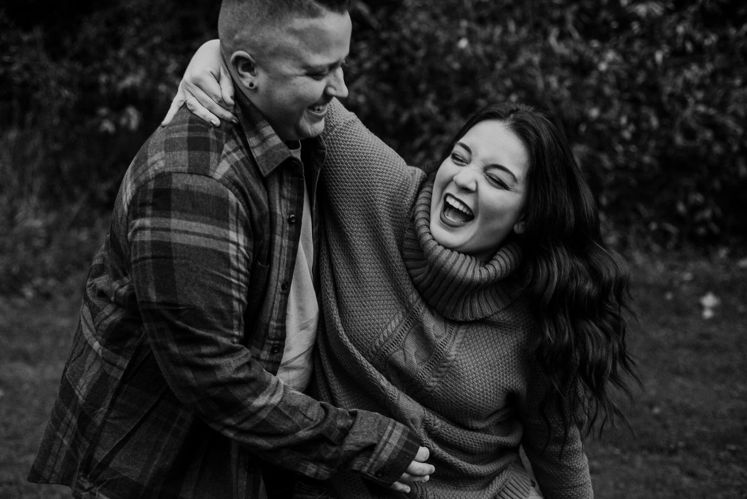 Queer couple laughing with arms around each other for engagement session
