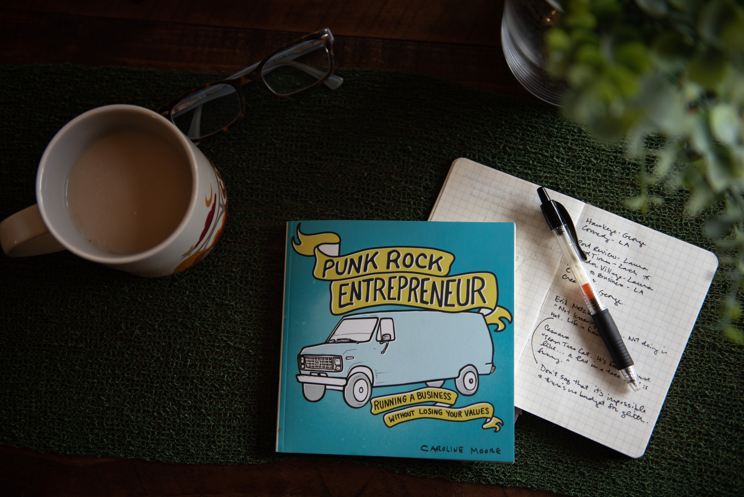A book, Punk Rock Entrepreneur, sits next to a coffee and an open notebook with notes