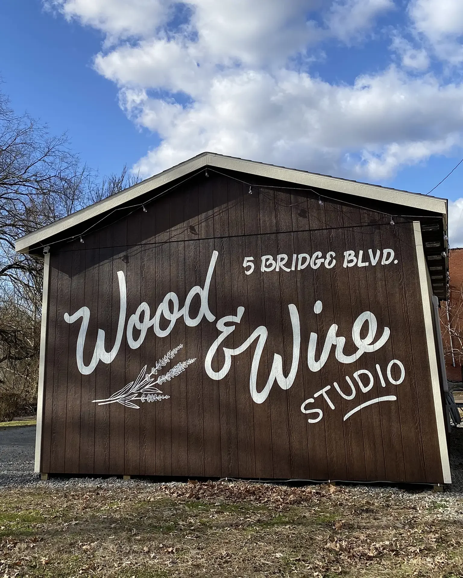 outside of our studio, a fancy shed. the sign says wood & wire studio, on a brown building with cream trim