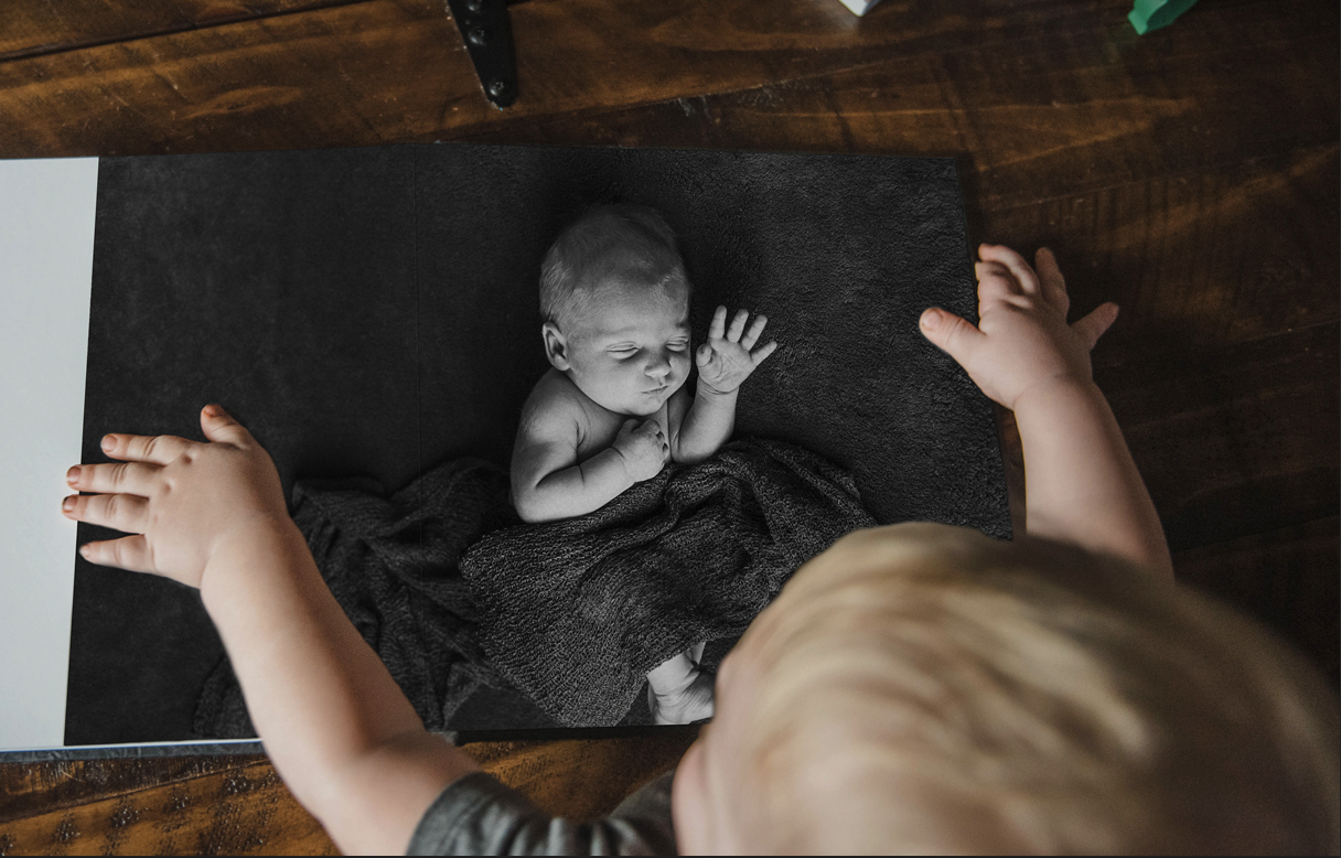 An album contains a photo of a newborn baby, the now older child rests his hands on the image