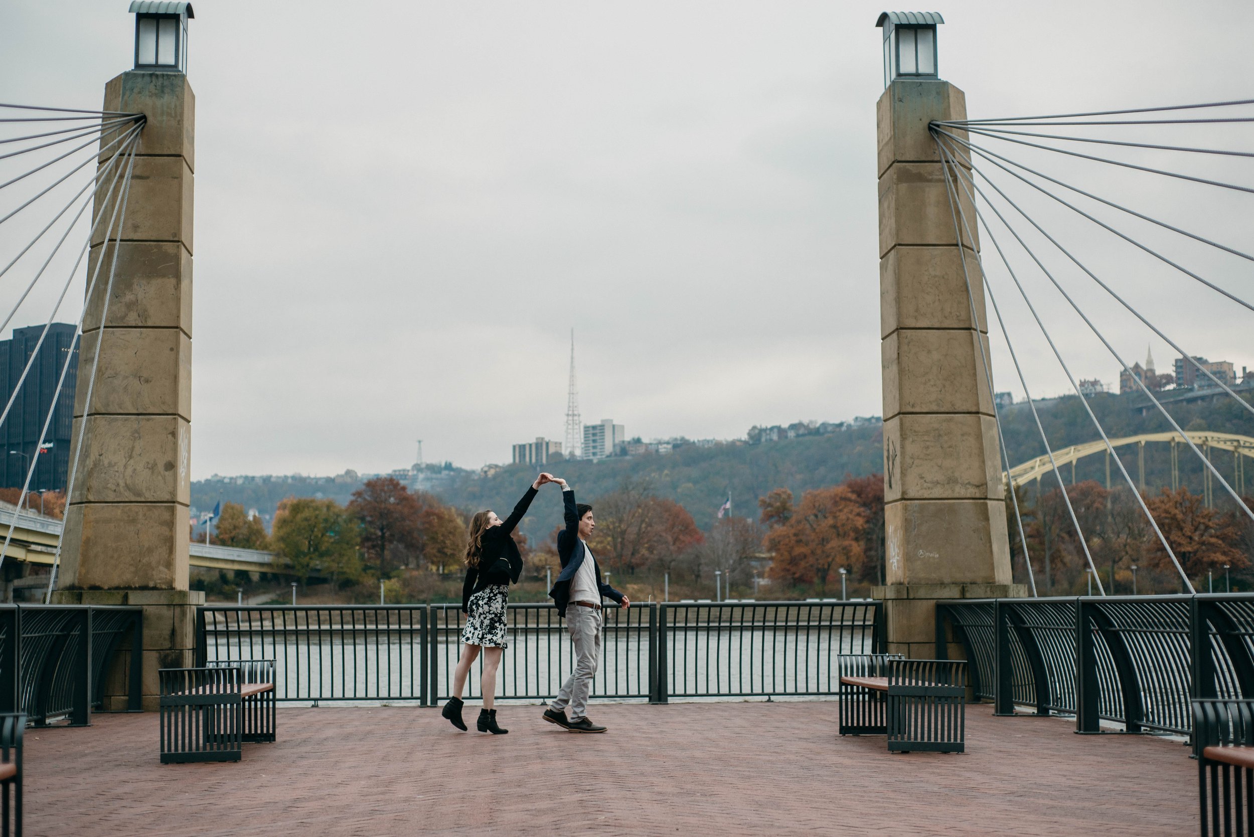 A woman spins her guy during their engagement session on Pittsburgh's north shore, they are standing between two large pillars