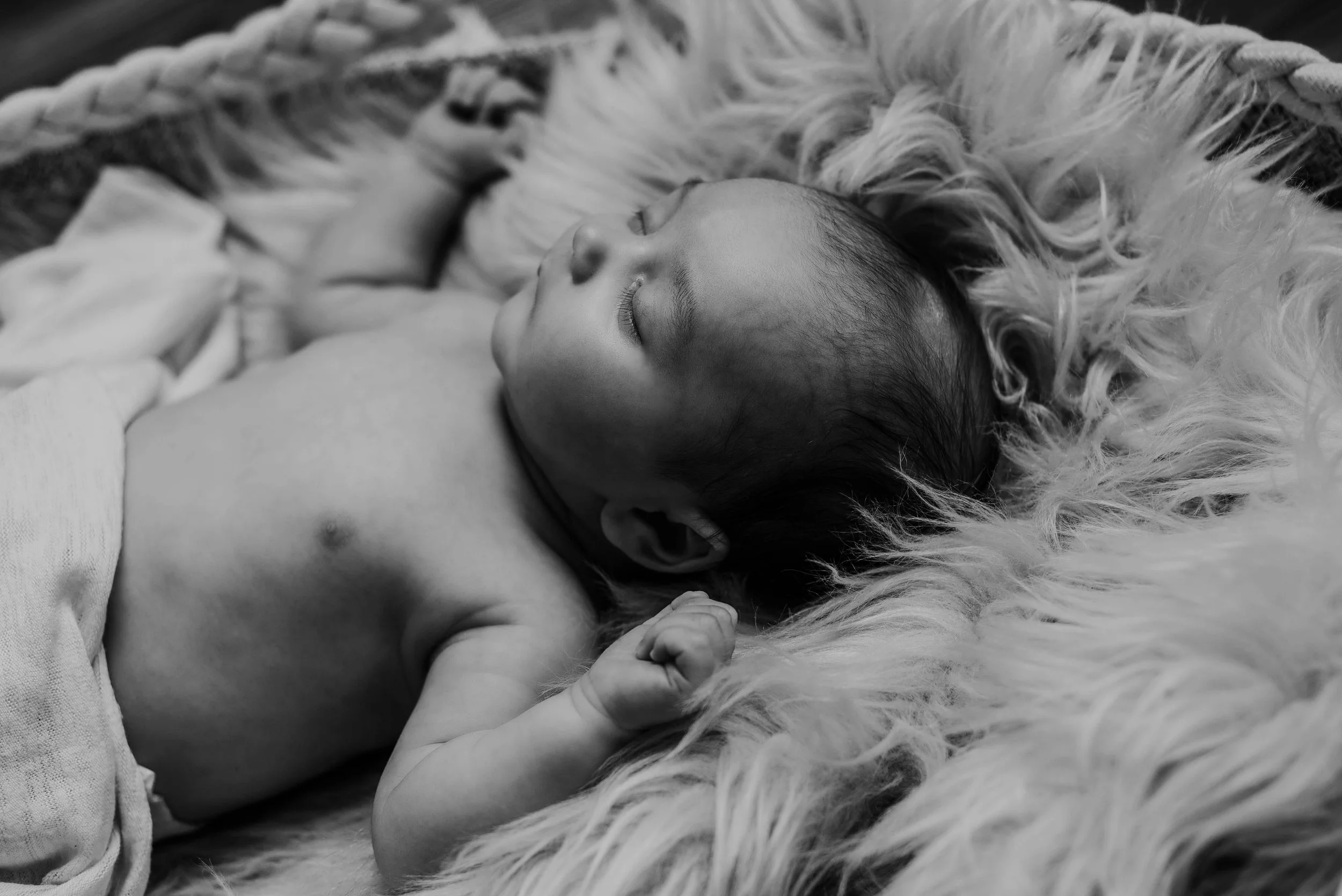 A sleeping newborn baby lying on a fuzzy blanket, with eyes closed and a relaxed expression. Studio newborn portrait, Uniontown PA.