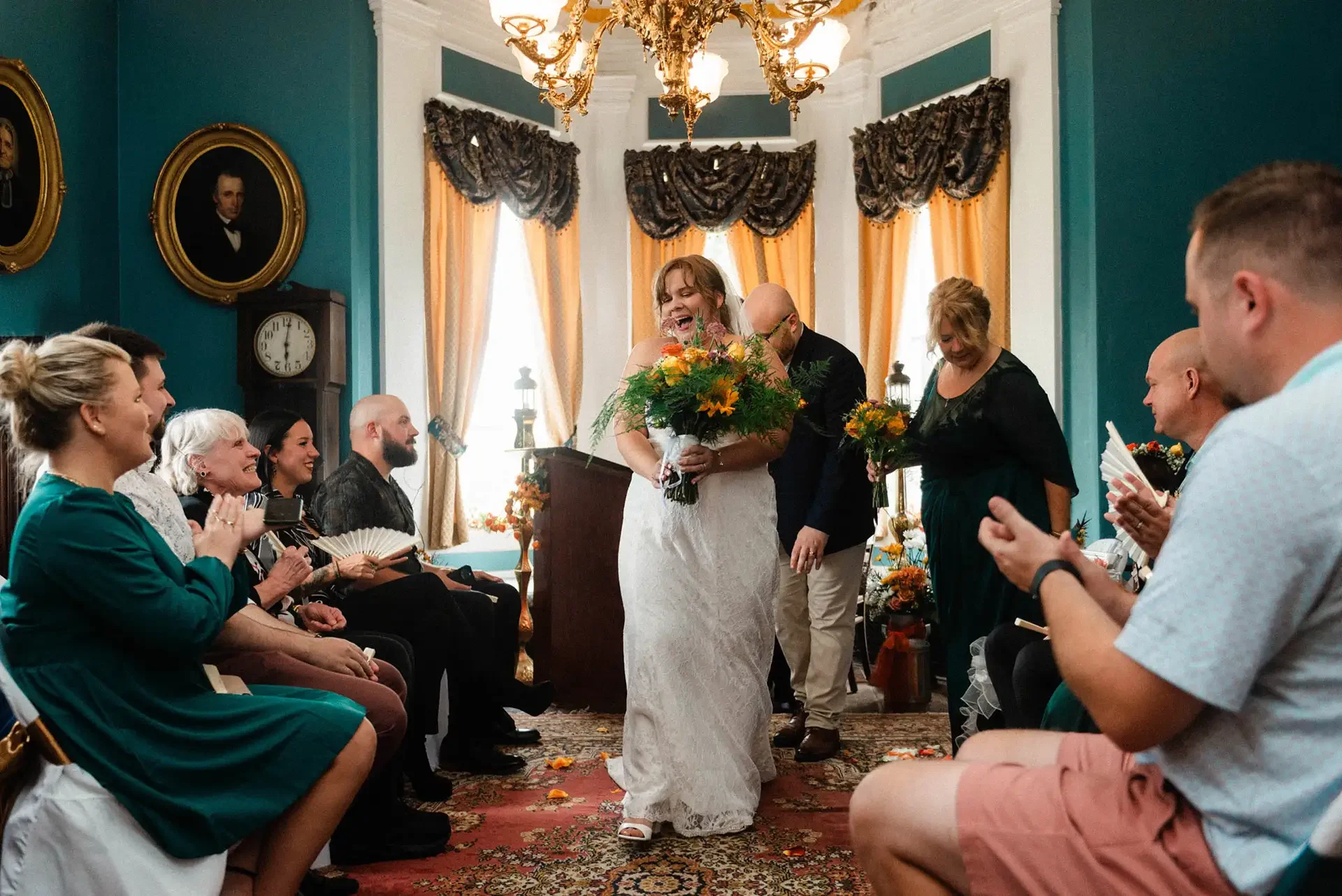 A newly married couple walks out of the room after they elope at Nemacolin Castle, the guests clap. They were married indoors in a blue room. 