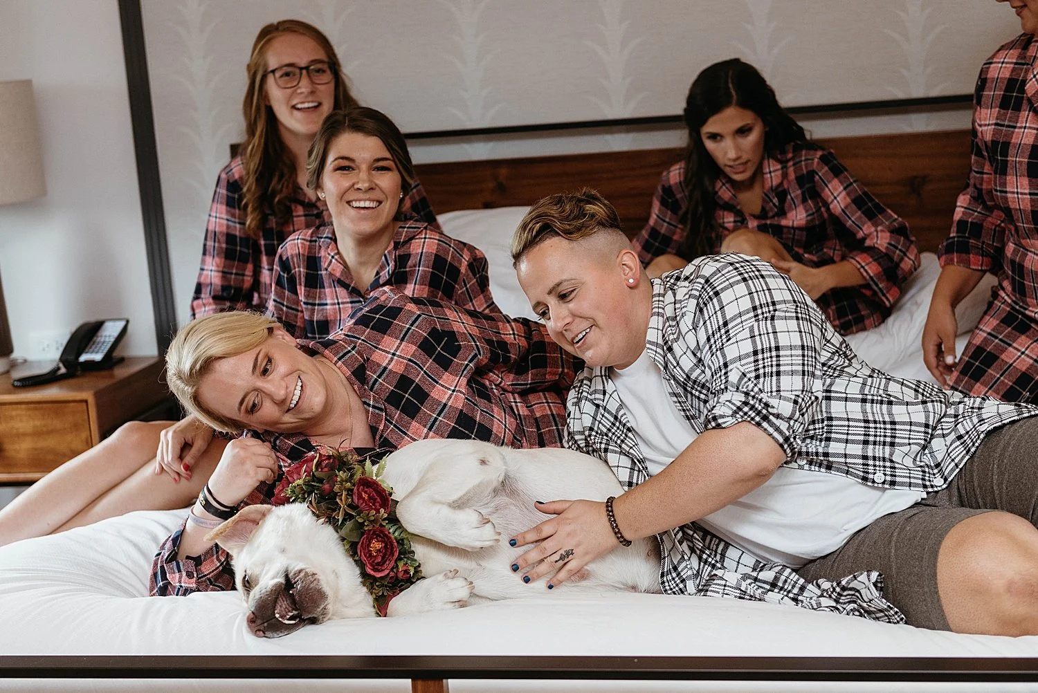 groom is on the bed with his wedding party and dog, they are all dressed in flannel shirts except the dog.