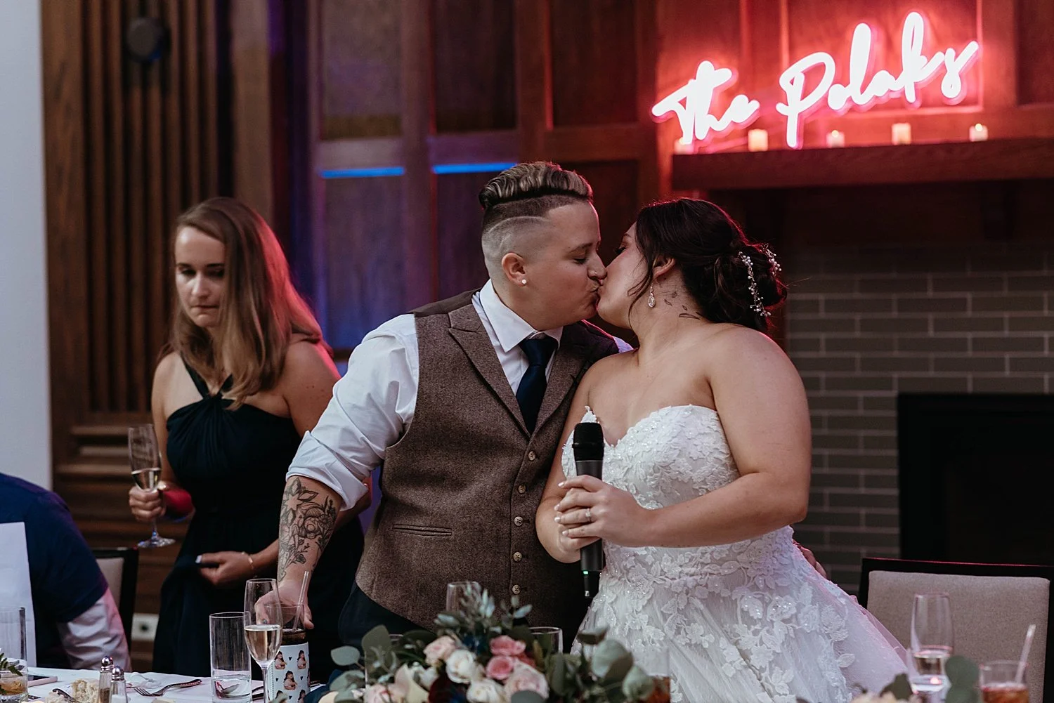 Bride and groom kiss at their reception table, set up in front of the tile fireplace at hotel morgan, and also in front of their lit neon sign of their last name