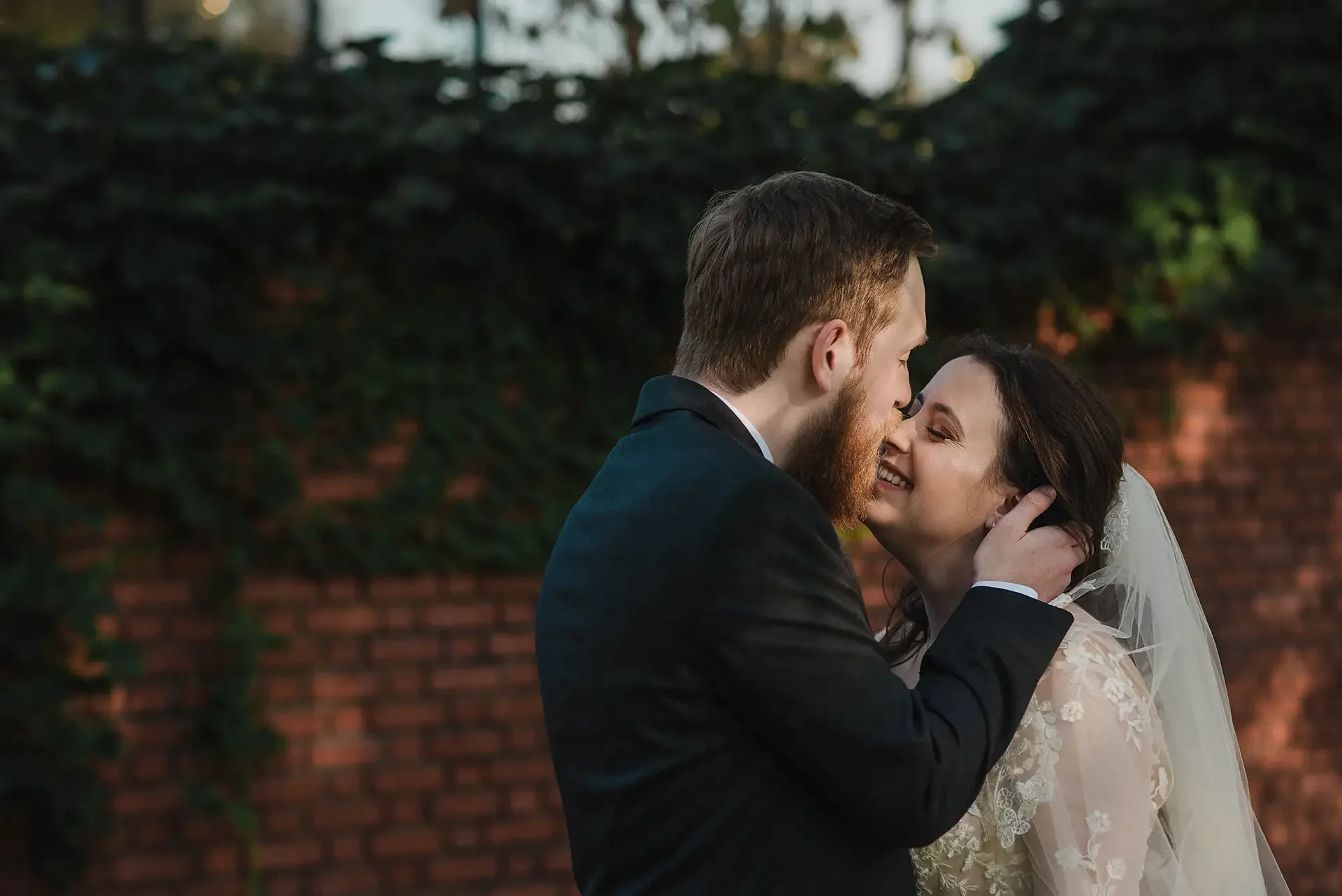 A bride and groom kiss in front of a brick wall with ivy after they elope at the Pittsburgh Aviary