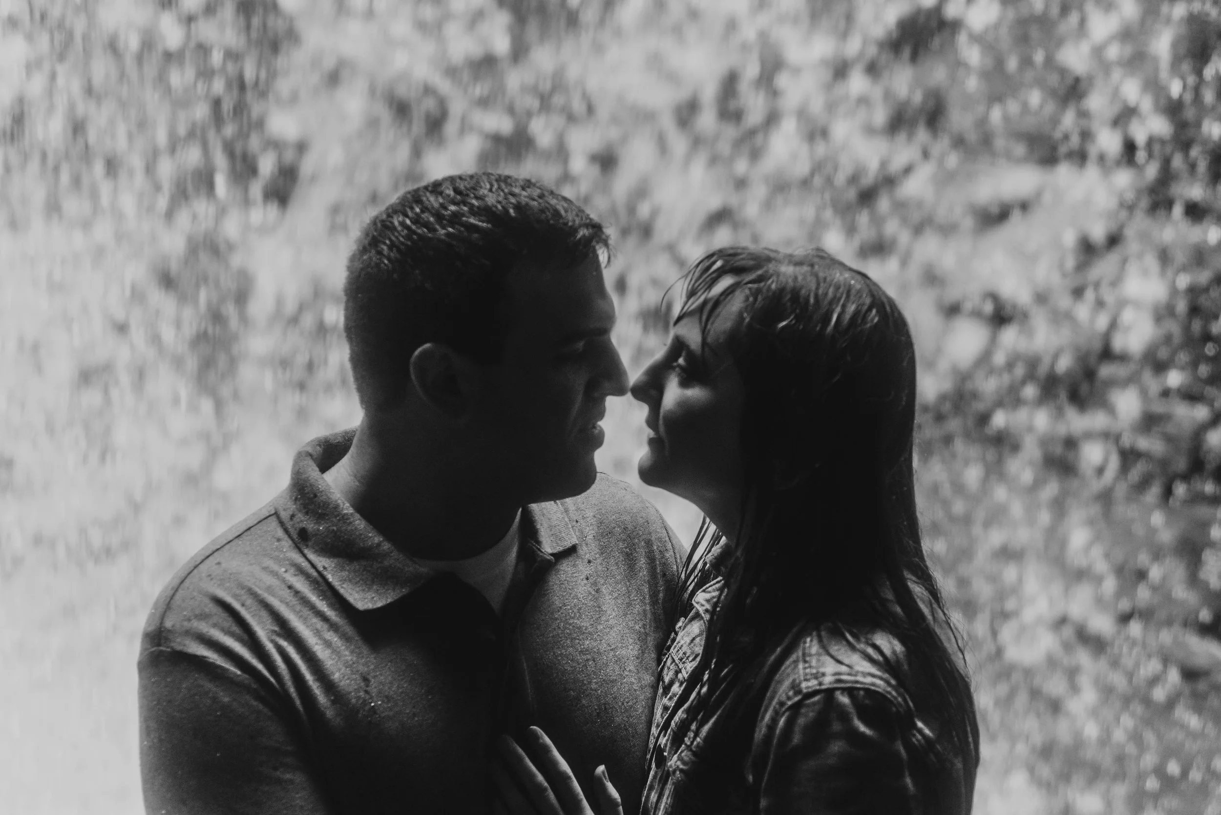 a couple stands beneath a waterfall at Ohiopyle, they are nearly kissing