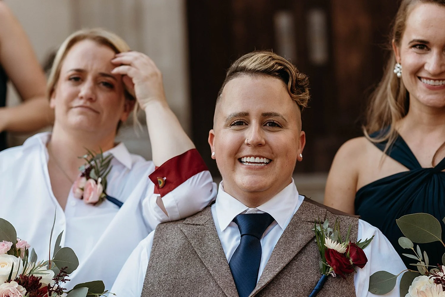close portrait of groom, his matron of honor rests an elbow on his shoulder