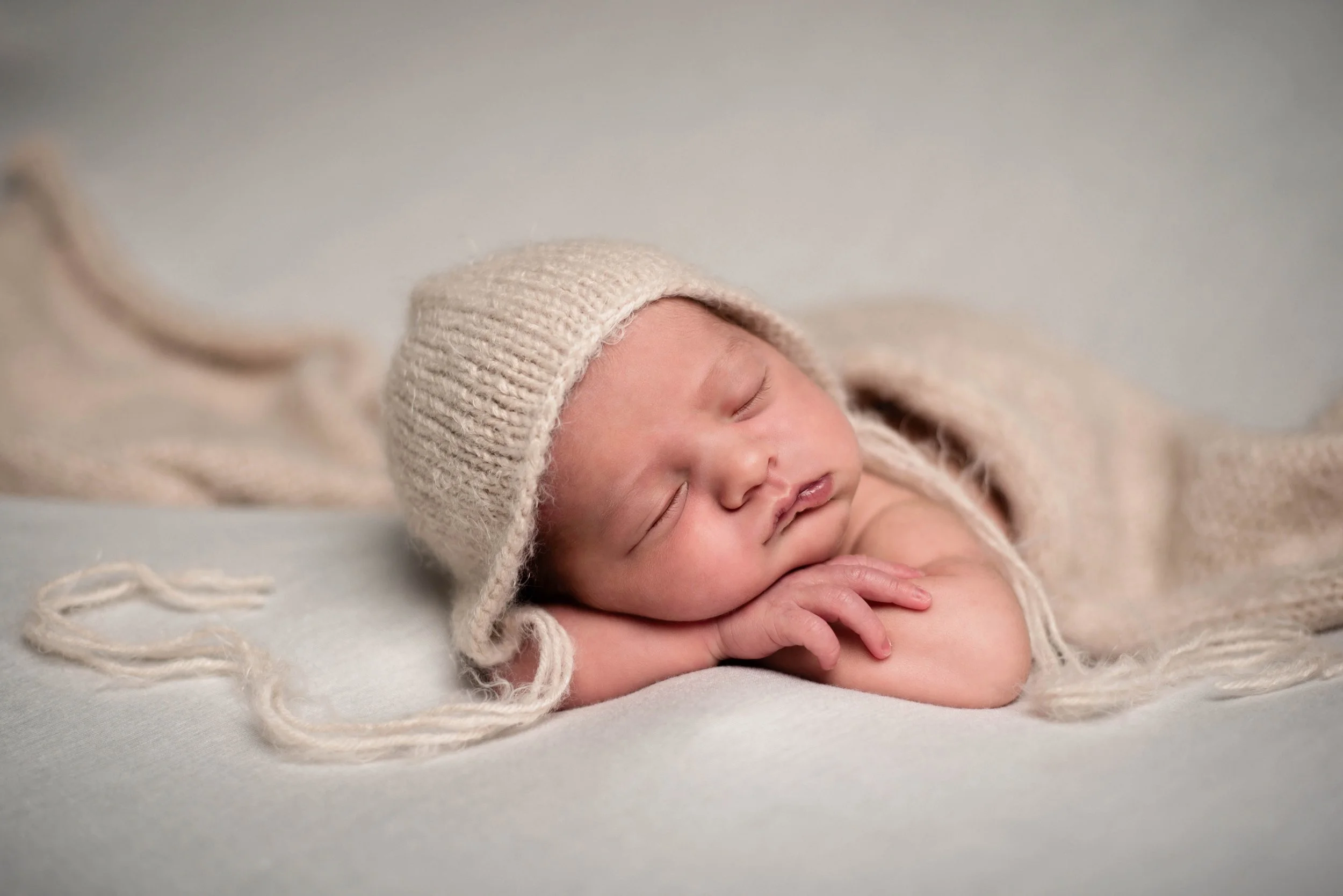 A sleeping baby with a knit hat, lying on a soft surface with hands under the cheek. Studio newborn portrait, Brownsville PA.