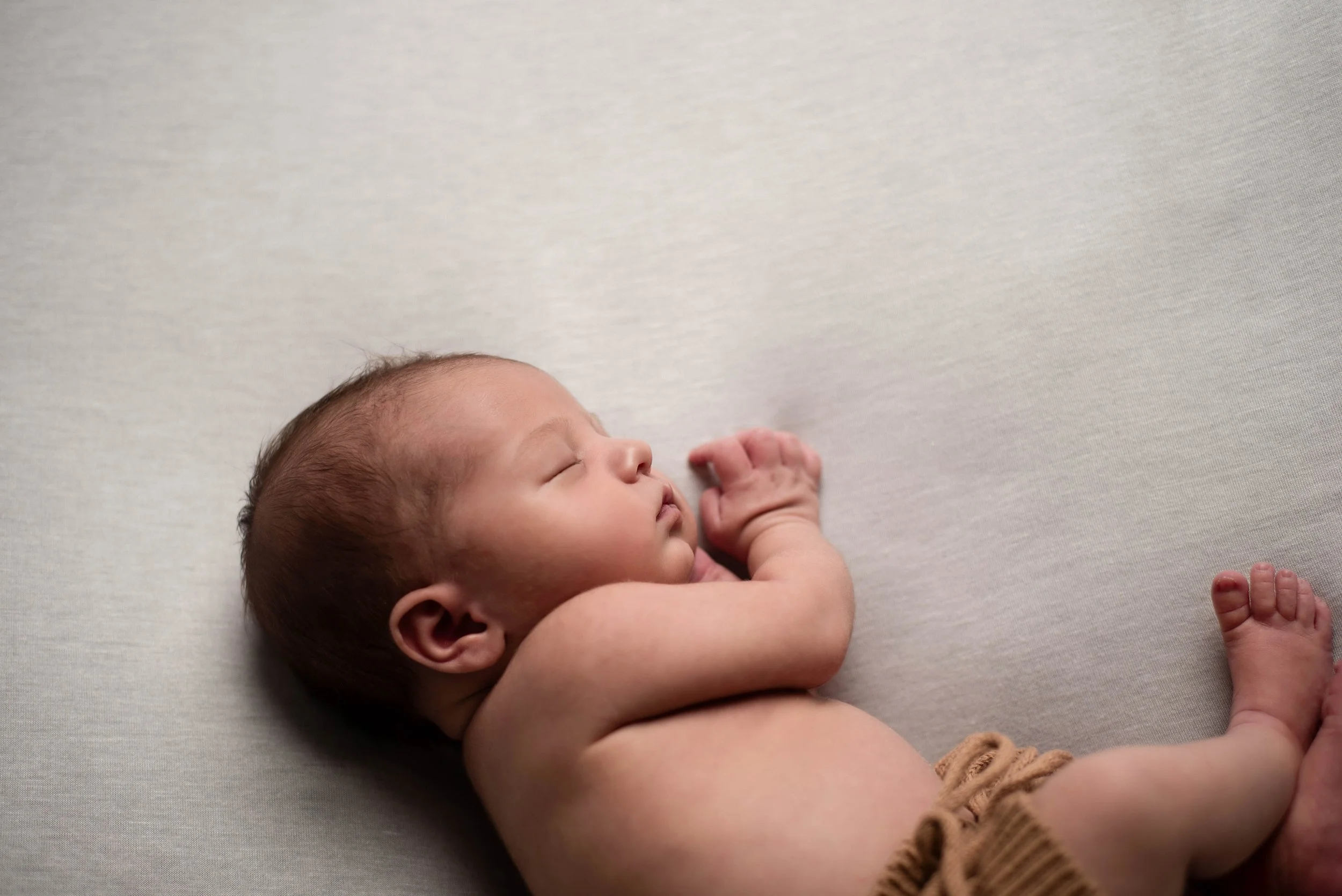 Close-up of a sleeping newborn baby lying on a light-colored surface, with arms bent and a peaceful expression. Studio newborn portrait, Uniontown PA.