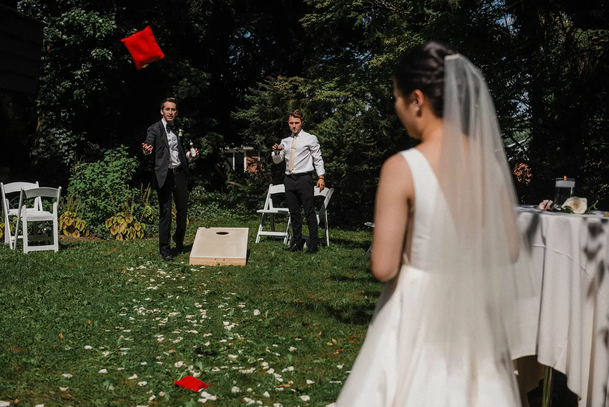 Bride watching groom and groomsman playing cornhole at outdoor wedding reception at the Hyeholde.