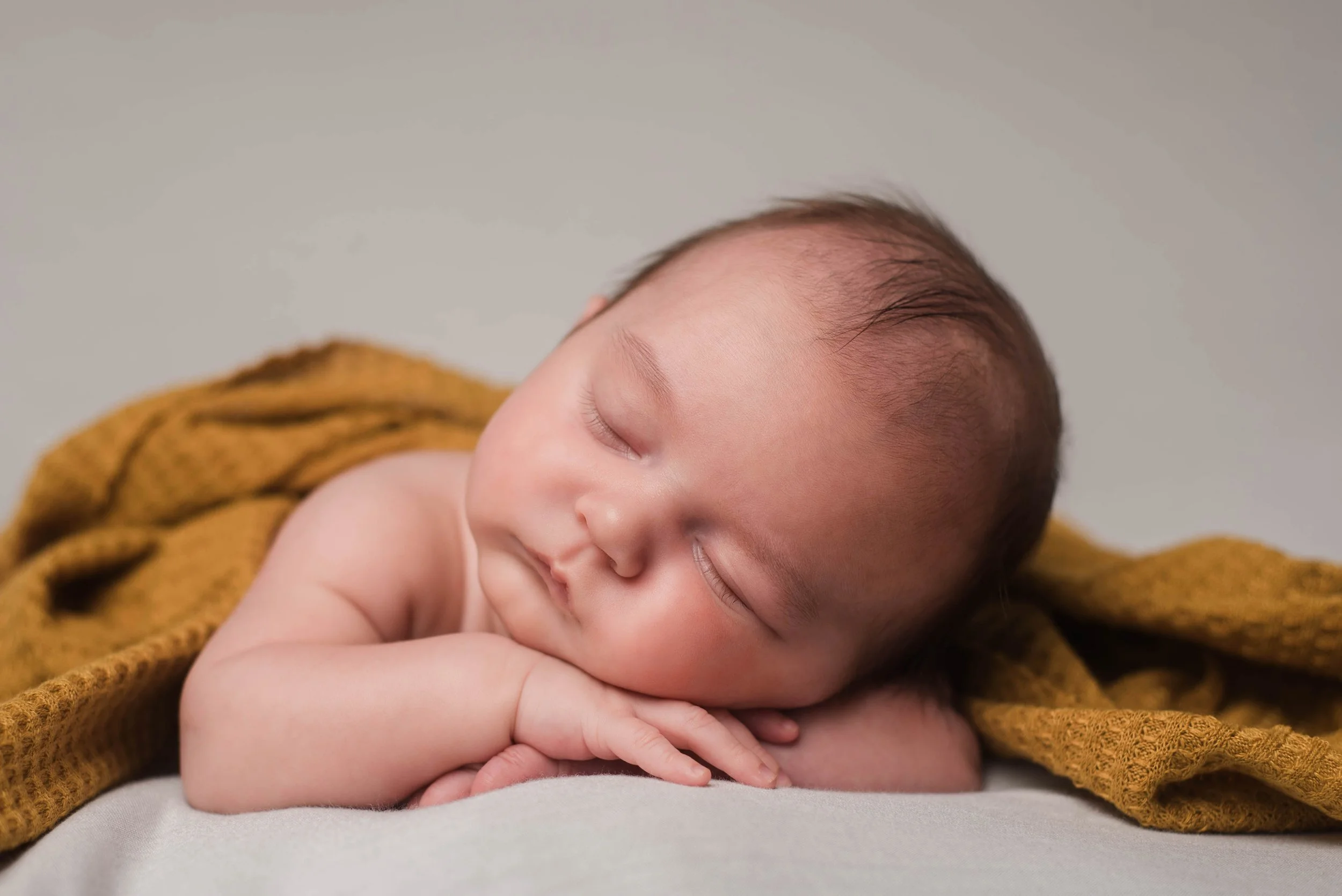 A sleeping baby with closed eyes, resting their head on their hands, on a soft surface, partially covered with a yellow blanket. Studio newborn portrait, Brownsville PA.