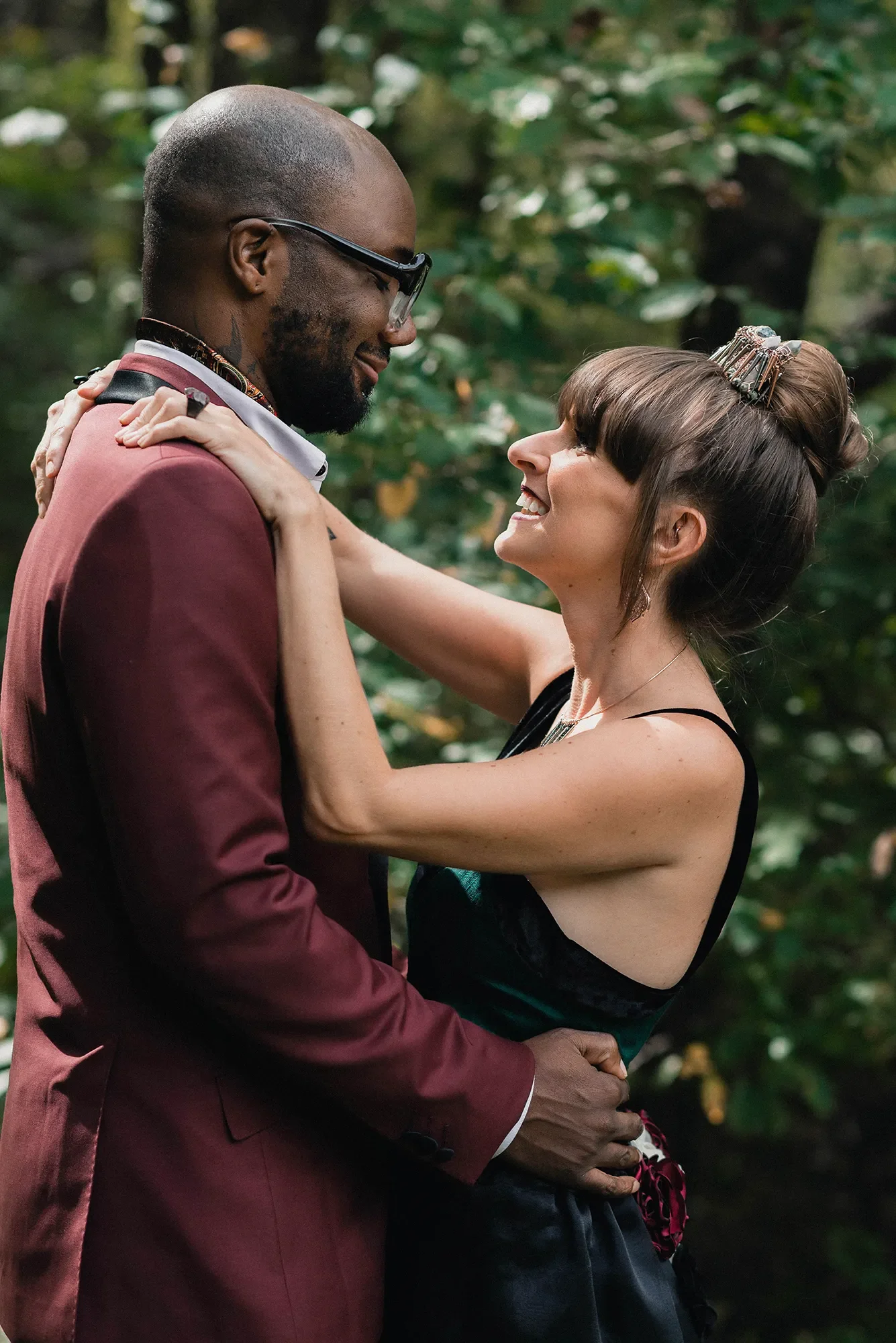 A couple embracing outdoors, smiling and looking into each other's eyes, with lush greenery in the background at their elopement in Raccoon Creek State Park, Pennsylvania