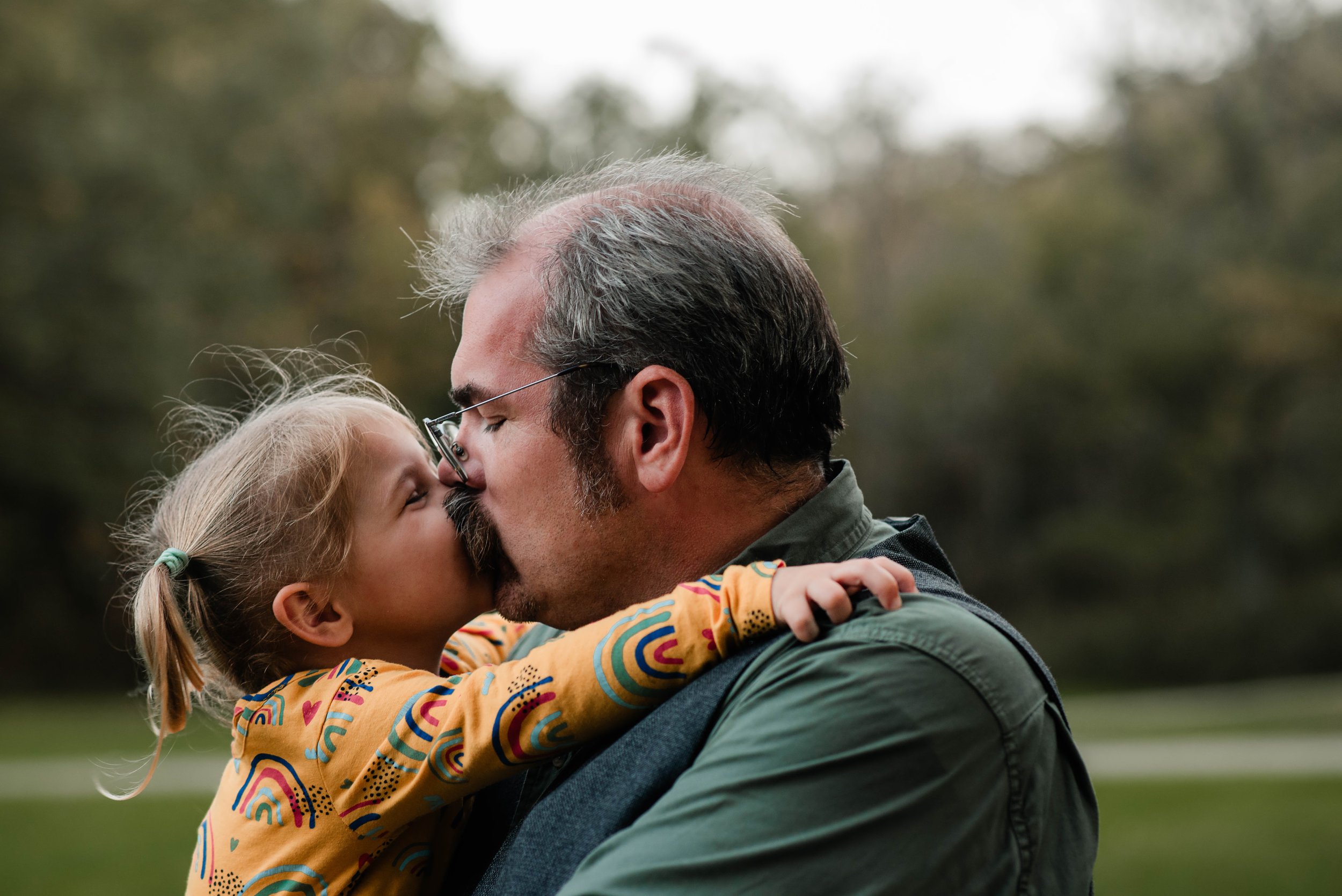 A family portrait session at Mingo creek park, a little girl gives her mustached dad a kiss