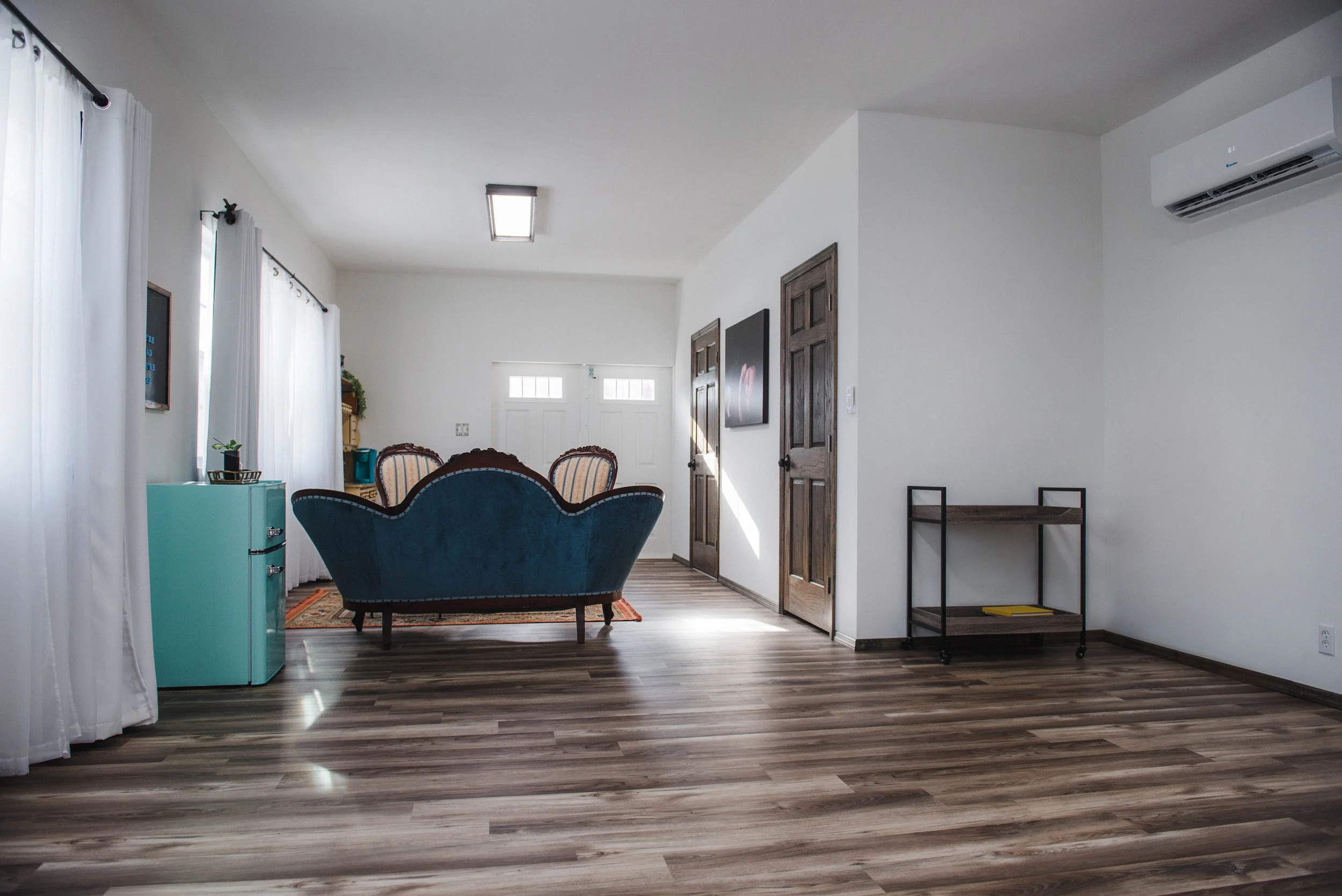 interior photo of wood and wire studio in west brownsville, white walls, wooden look vinyl floor, vintage blue couch, and huge windows