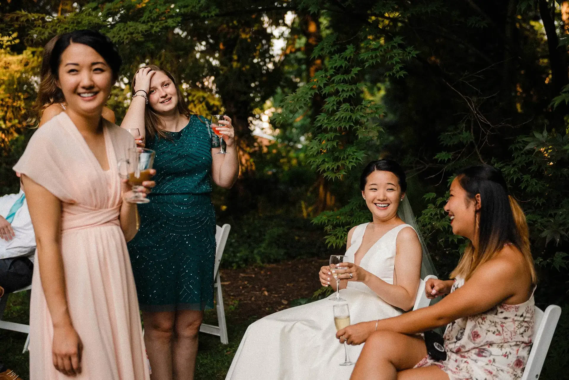 A bride sits casually with a glass of wine, talking to friends in the courtyard at the Hyeholde after her micro wedding
