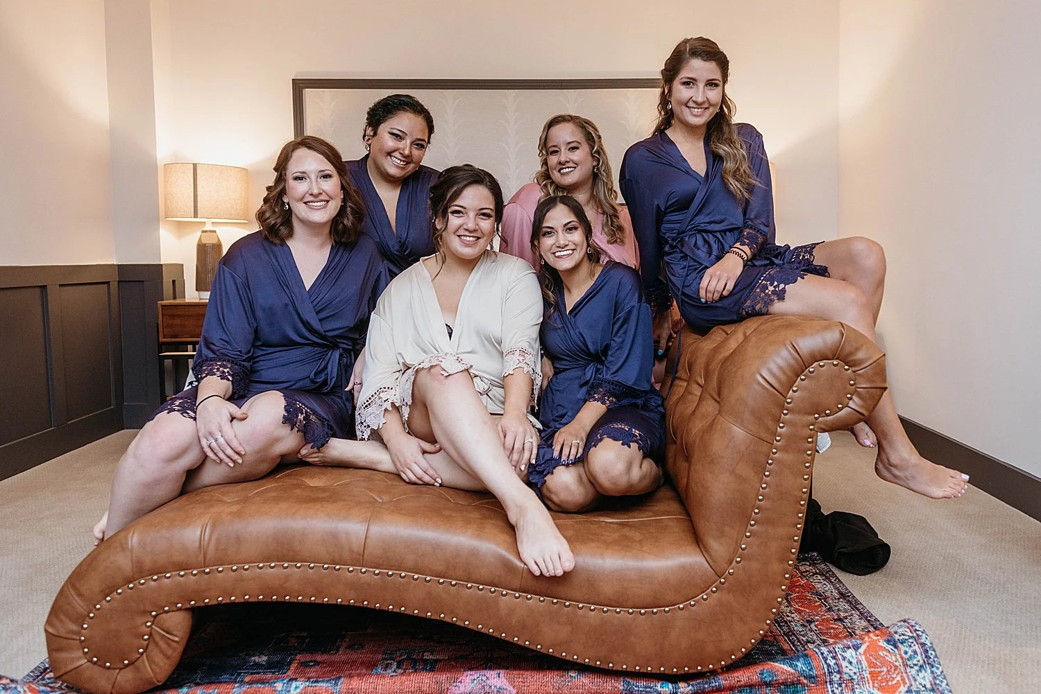 Bride sits with her bridesmaids on a leather chaise in a hotel room at Hotel Morgan