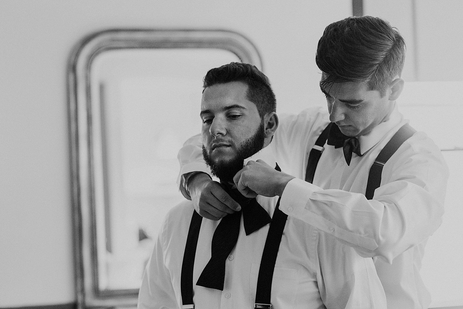 Groomsman helping another groomsman to tie his bow tie