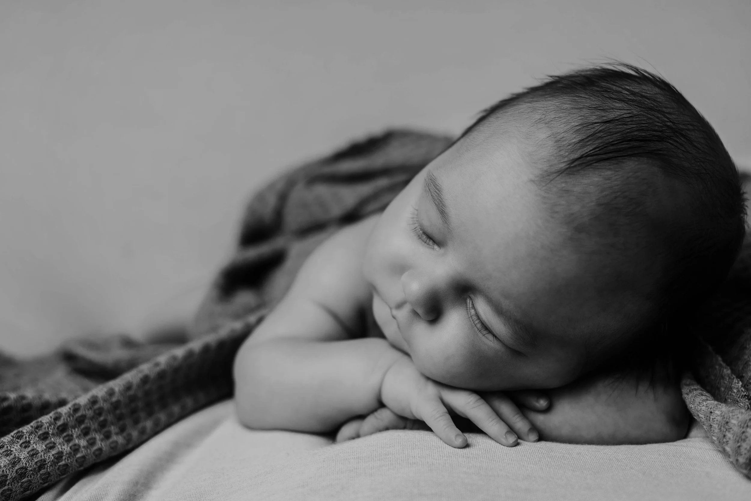 A sleeping young child with short hair rests on a pillow, partially covered with a blanket, in a black and white photograph. Studio newborn portrait, Uniontown PA.