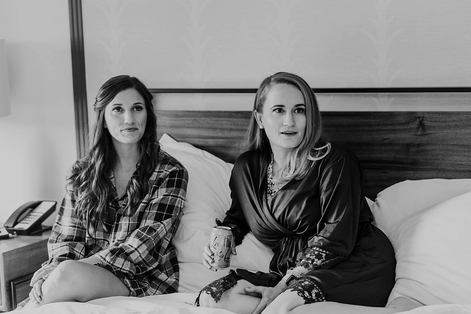 Ladies in the wedding party sit on a bed at the hotel morgan. one is in a flannel shirt, the other in a robe.
