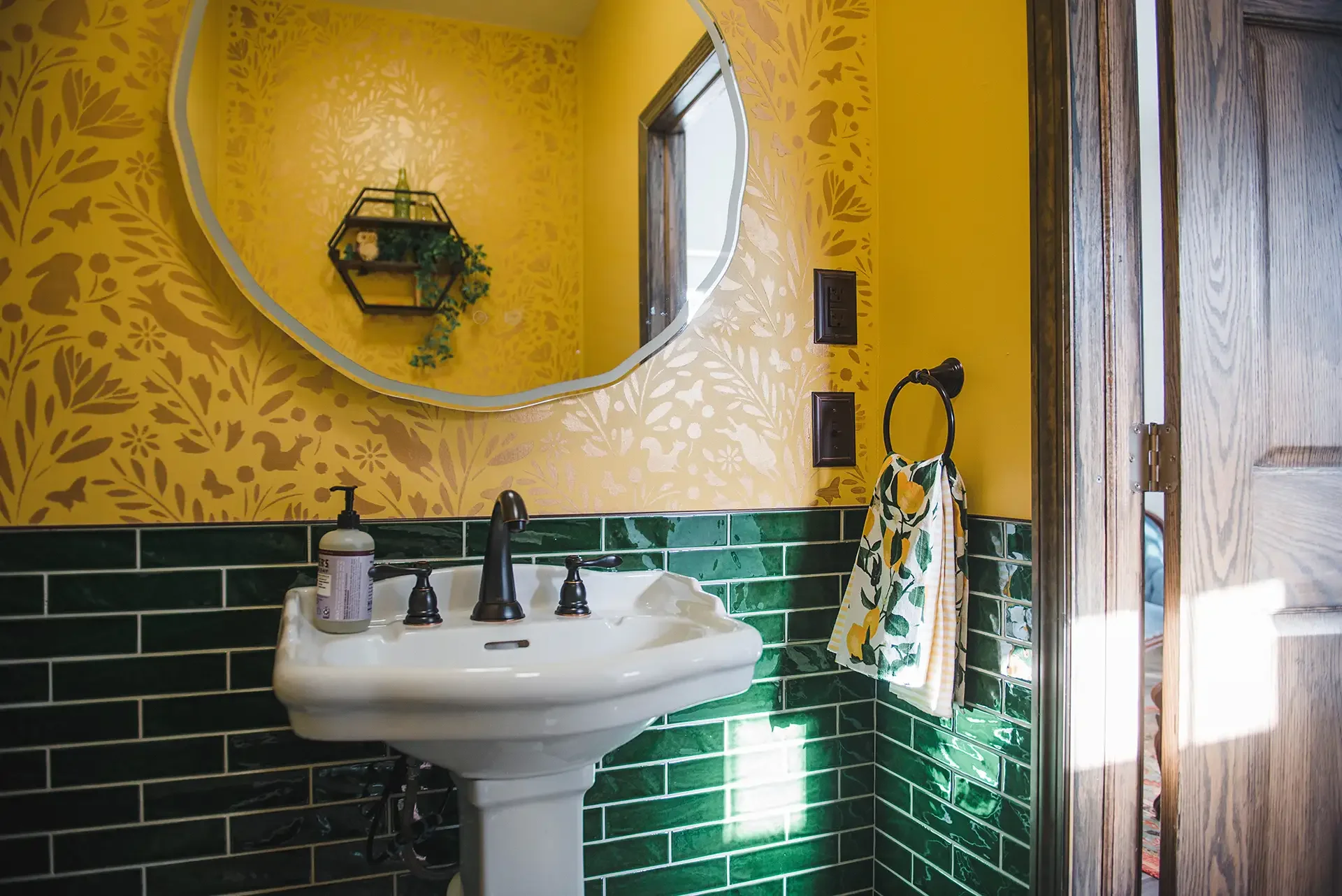 the bathroom sink, in front of green subway tile and a gold hand stenciled mural with bunnies and foxes