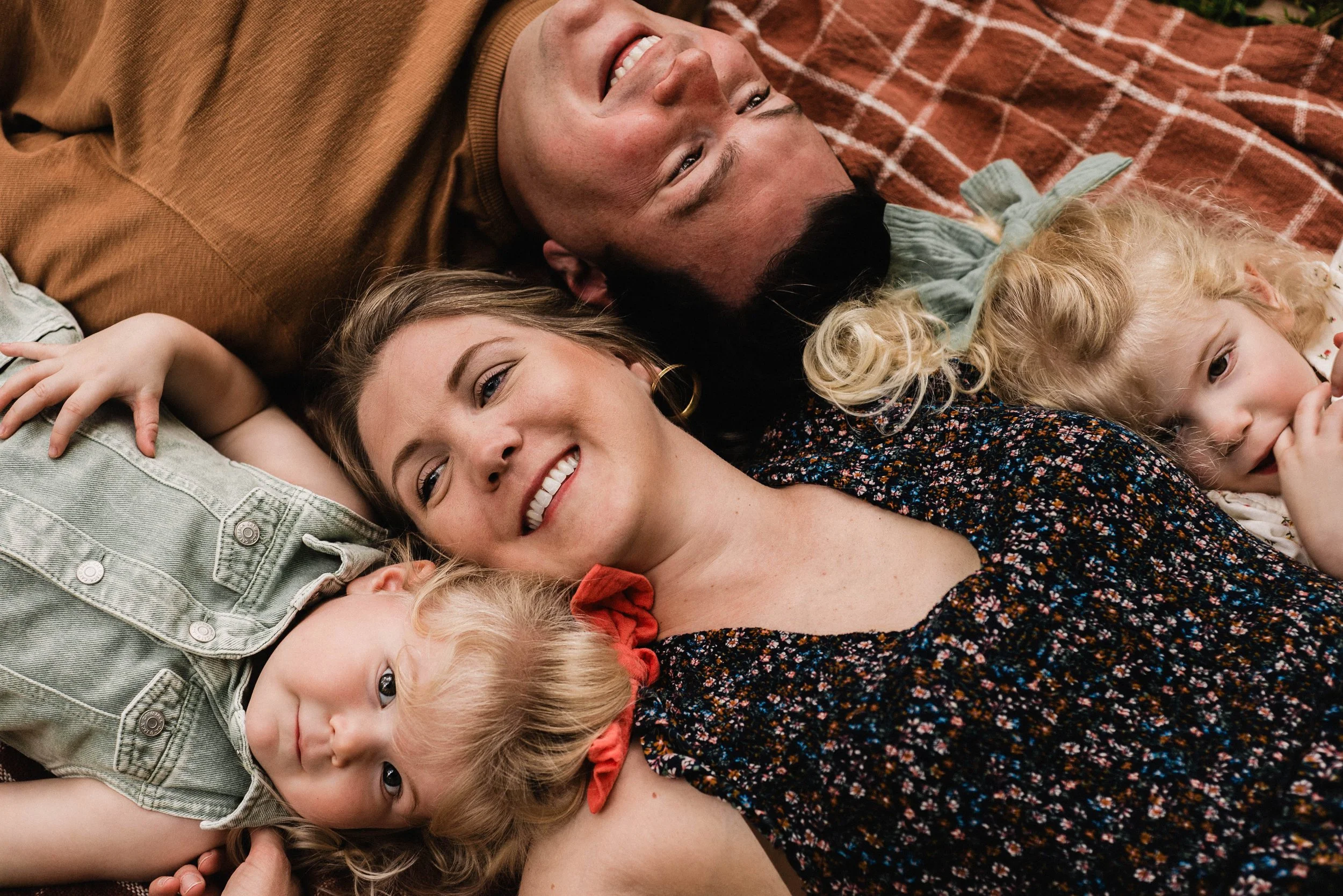 A family of four lays on a blanket, their heads all close together