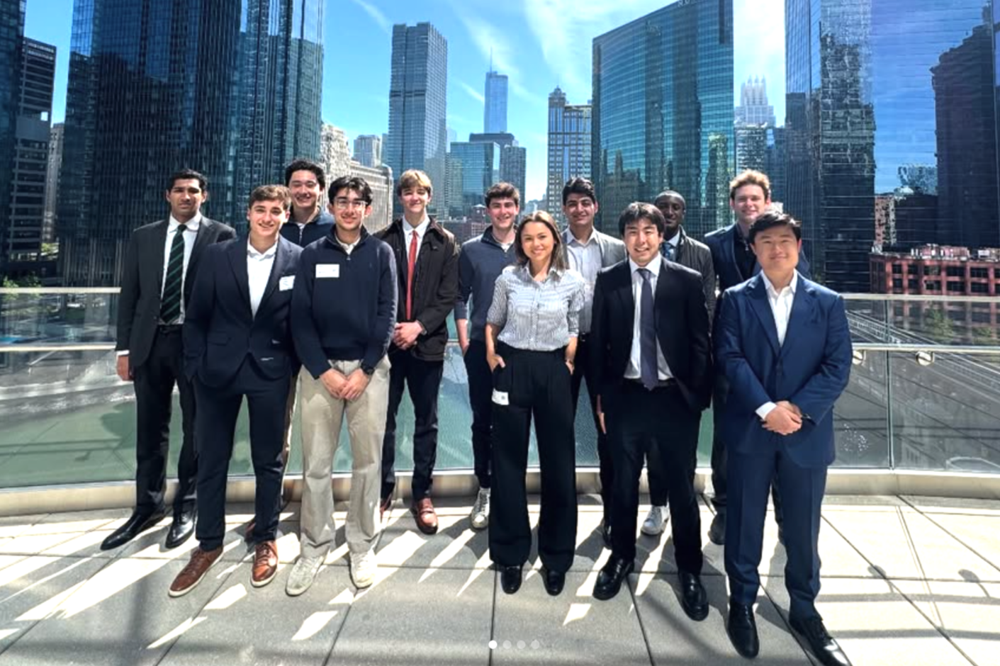 Group of professional people posing on a rooftop with a city skyline and tall buildings in the background.