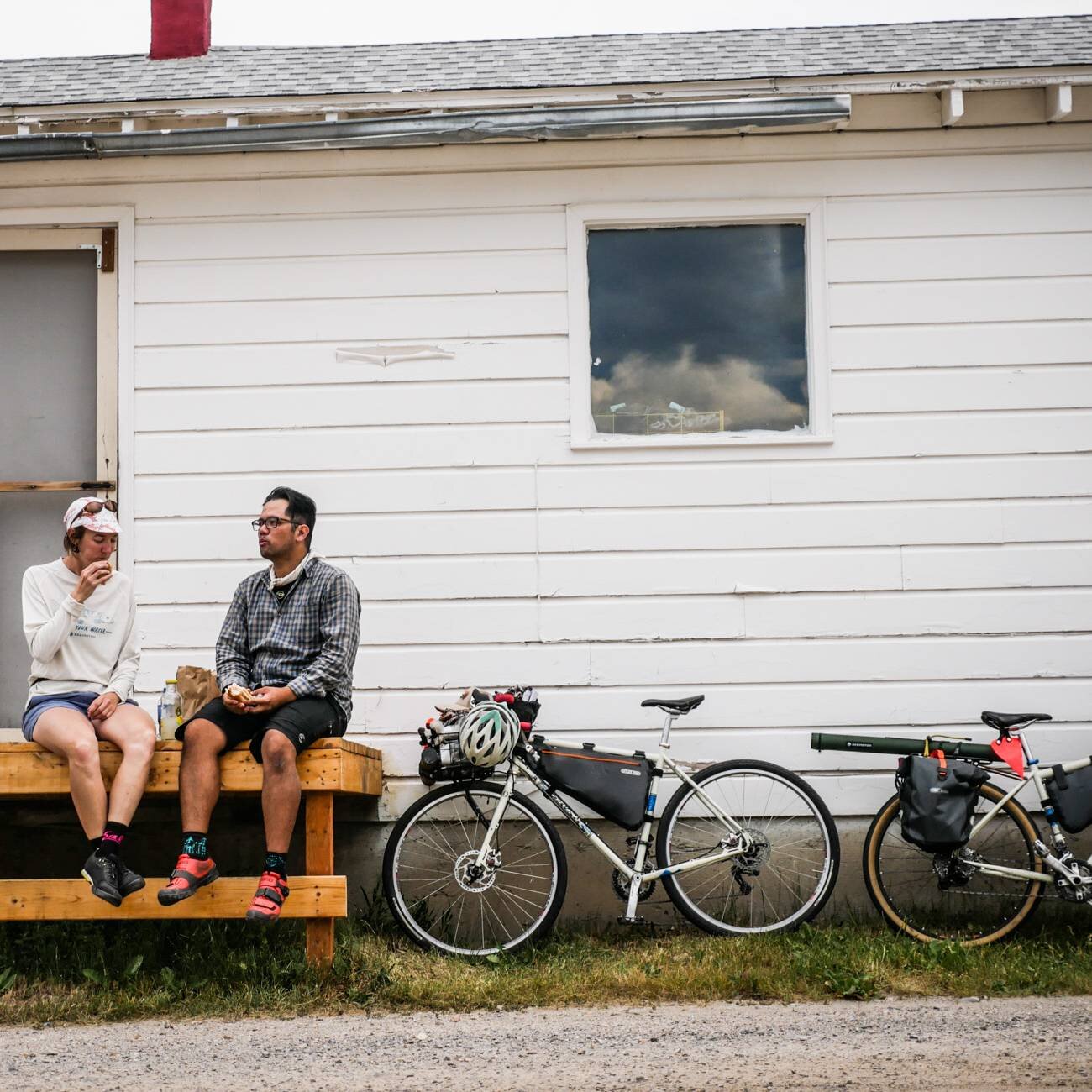 Two cyclists sit outside of a small town market with their bicycles.