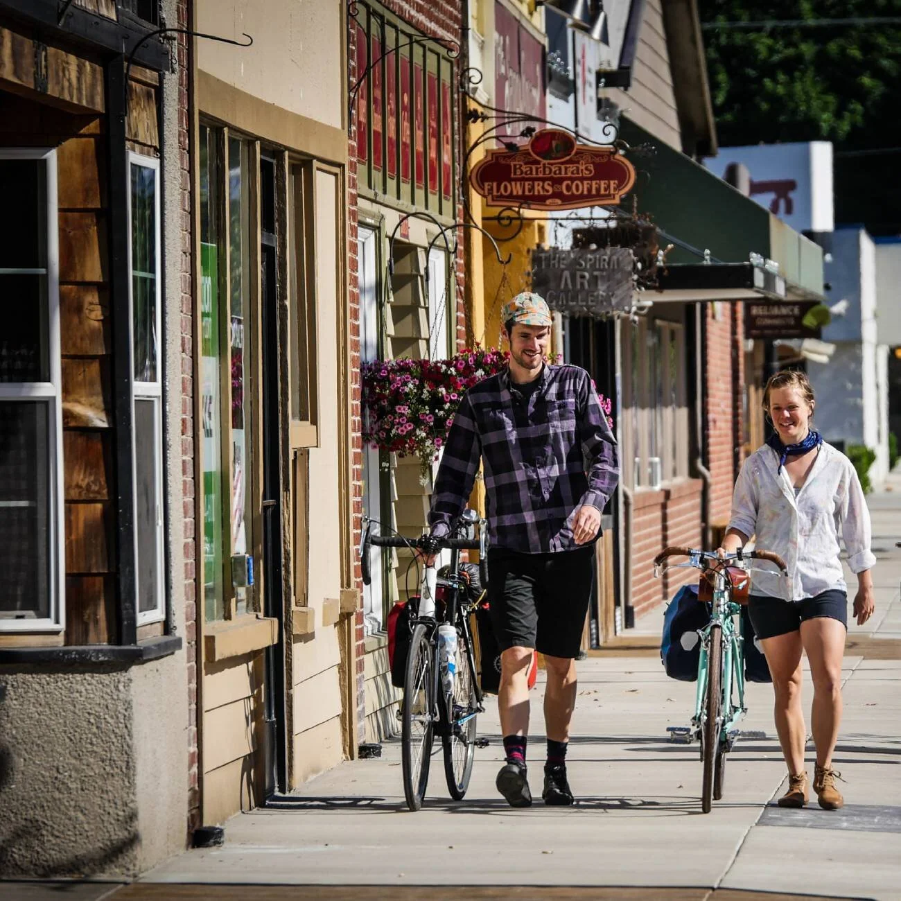 Two cyclists walk with their bicycles along a rural mail street.