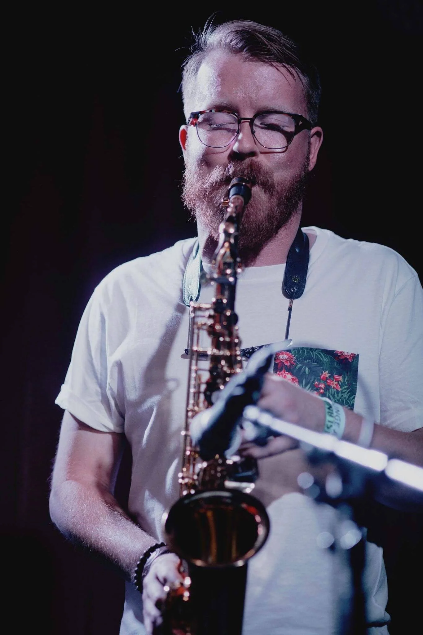 A man with glasses and a beard playing a saxophone.