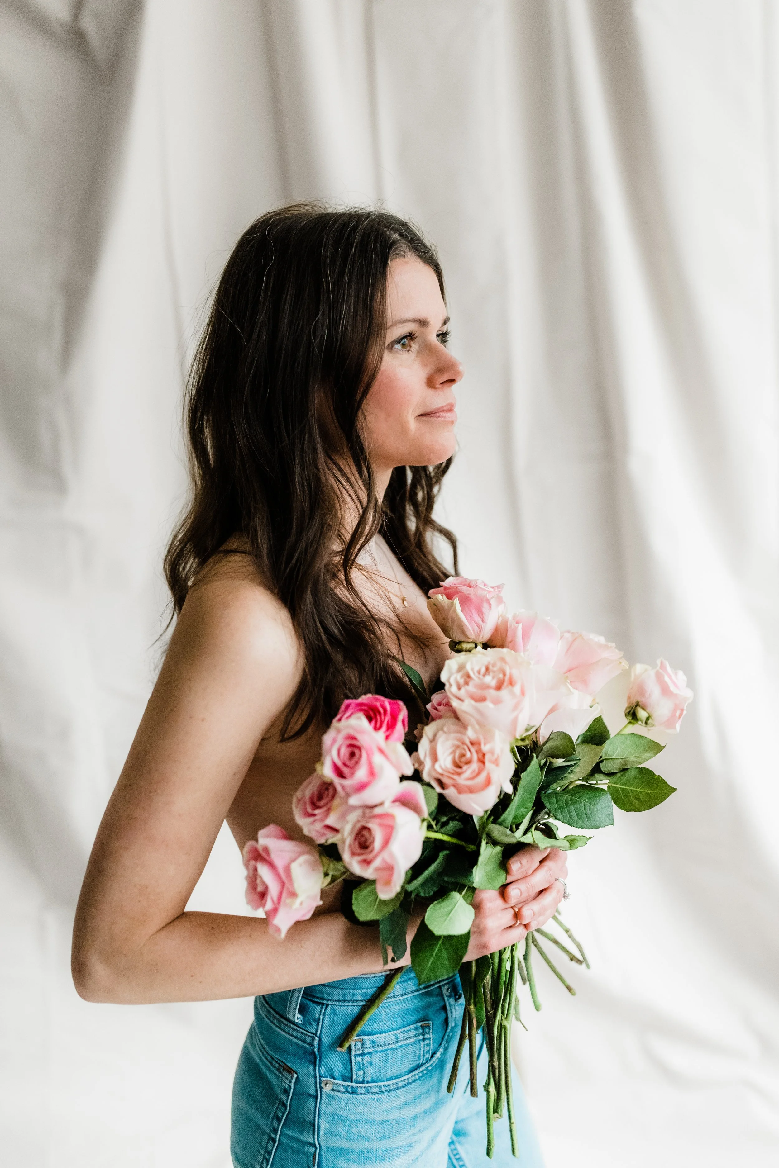 woman facing to the side, holding pink roses over her chest