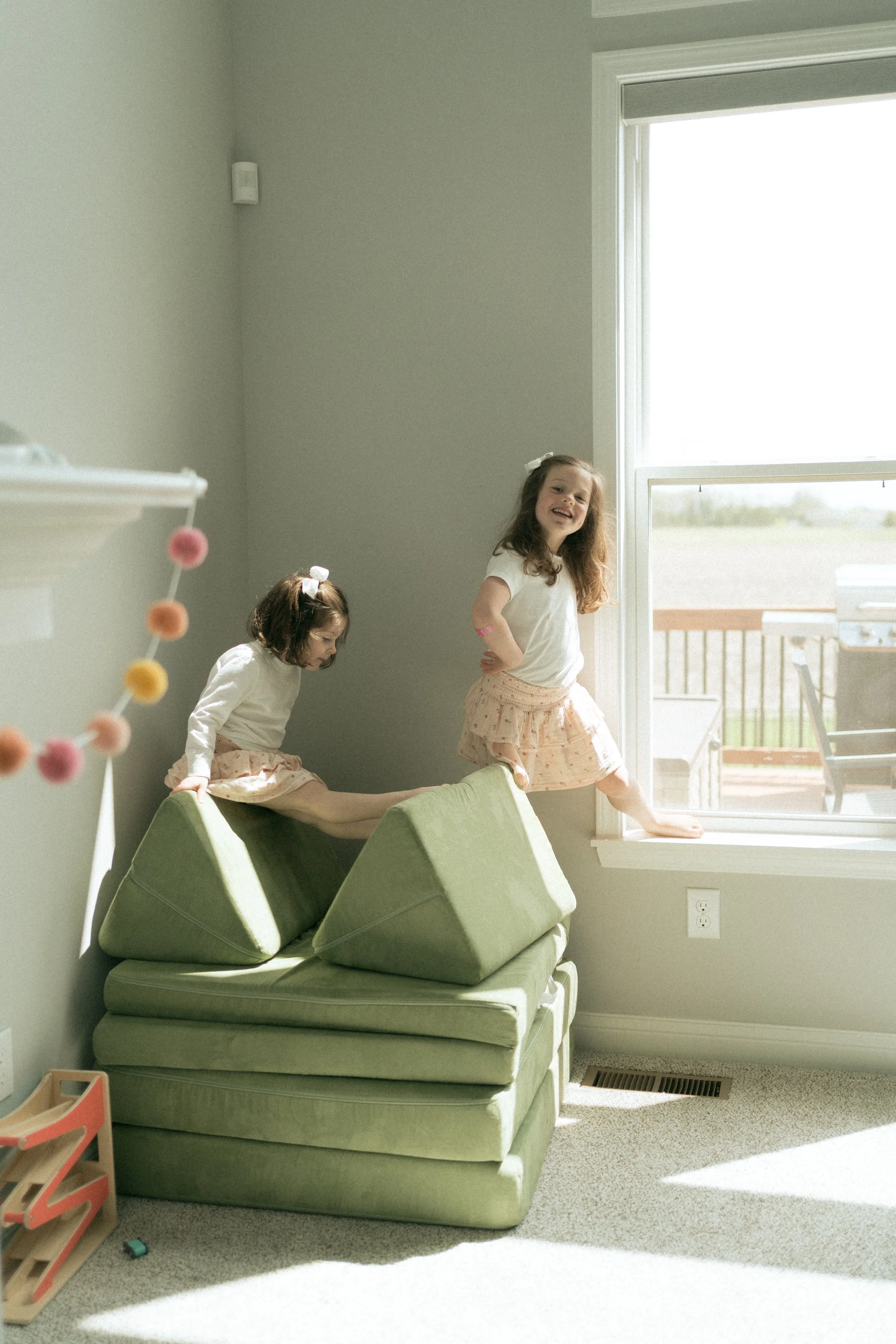 Two young sisters playing on play couch in living room