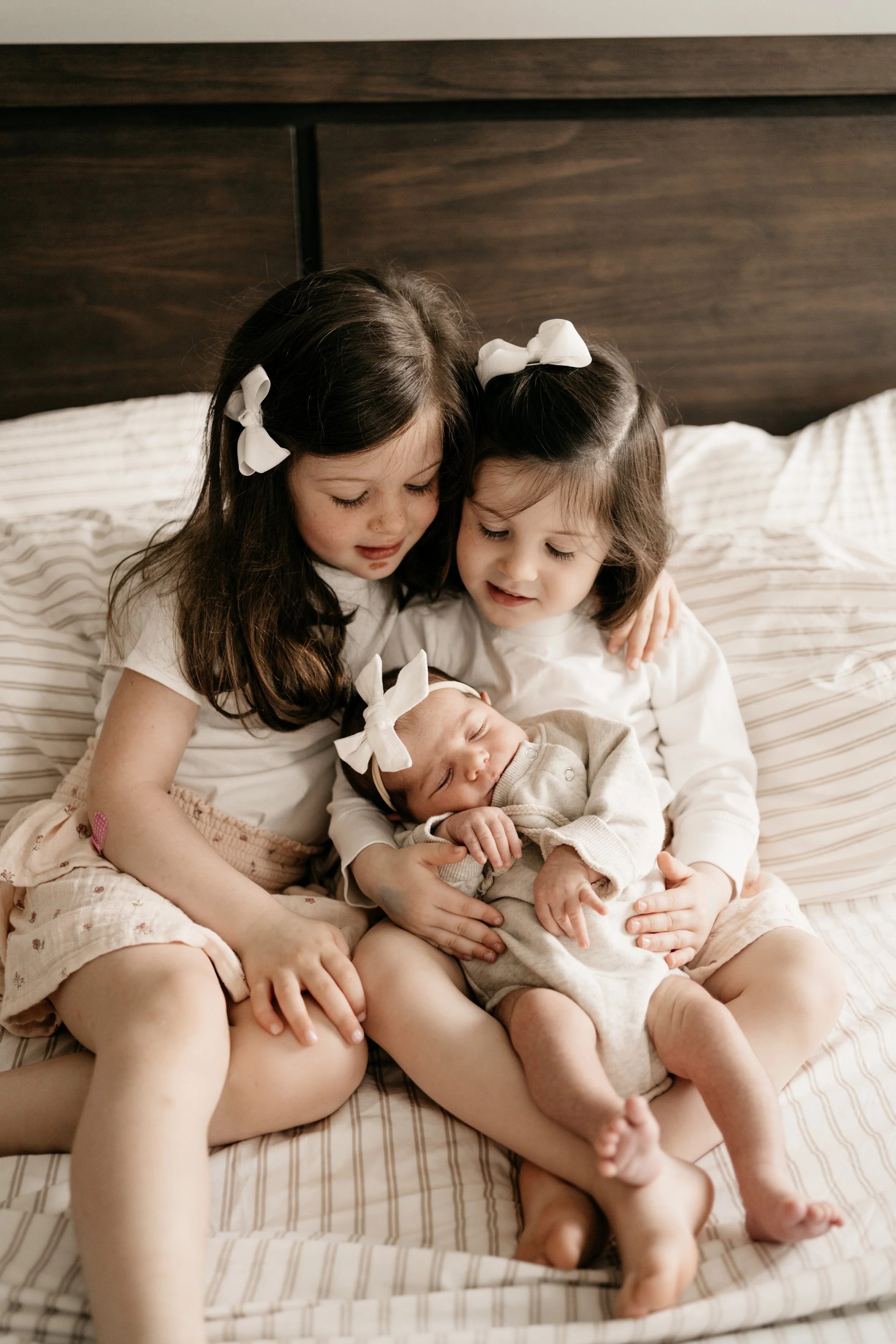 Two young sisters holding newborn baby sister in bed