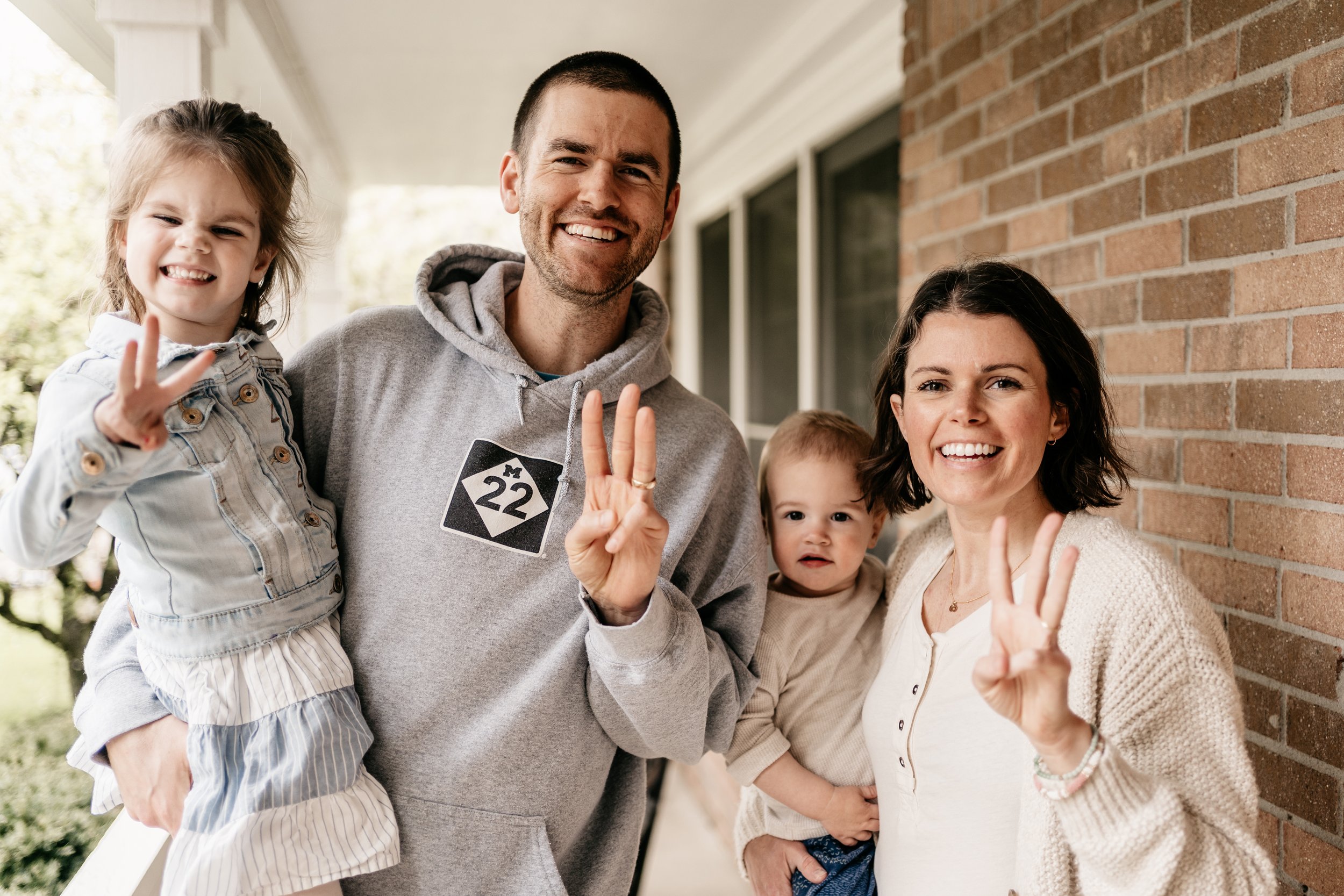 father, woman with cancer, young daughter and baby son, holding up 3 fingers for finishing third chemo treatment