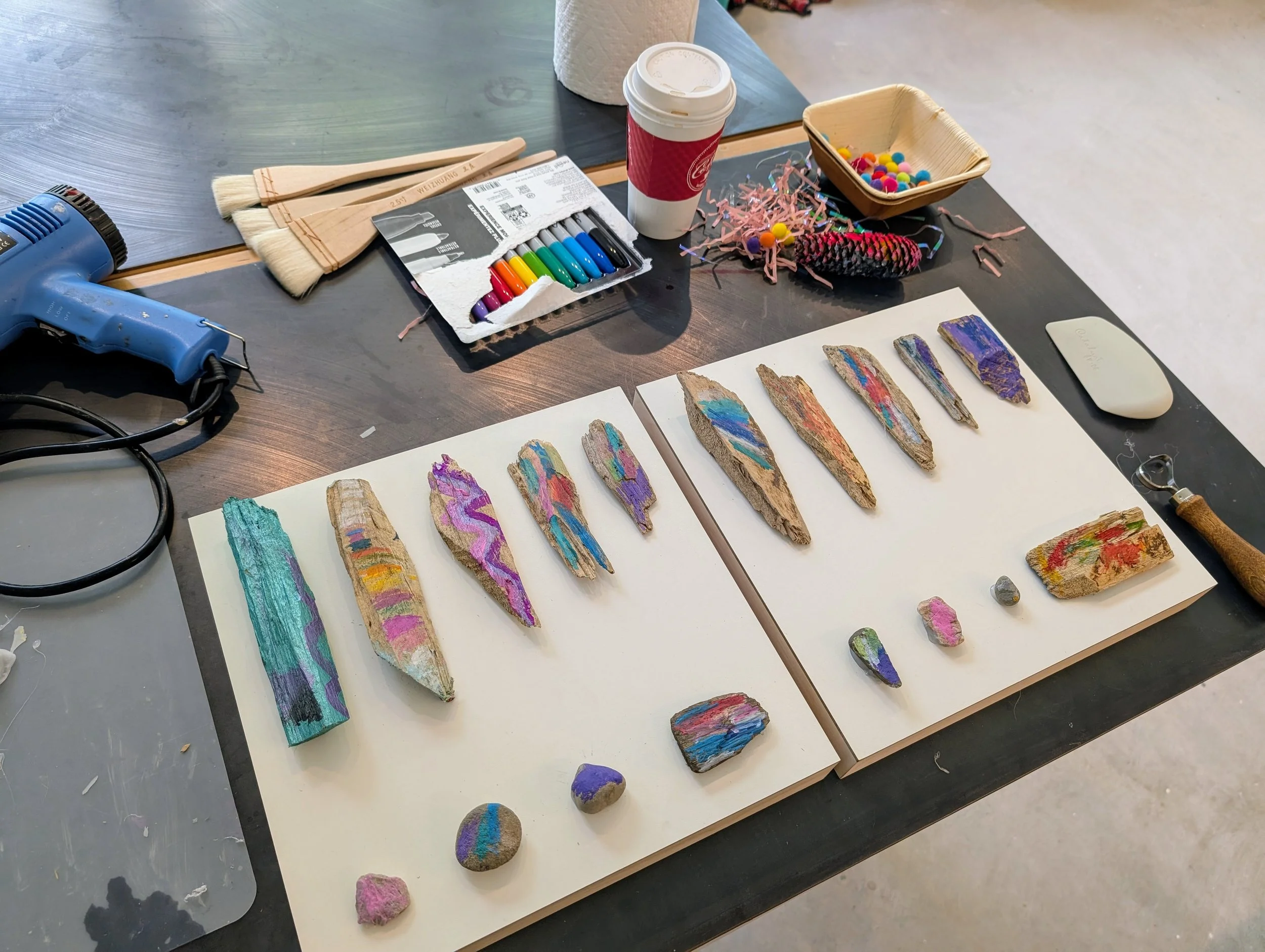 Studio workspace with painted rocks, art supplies, and tools on a table.