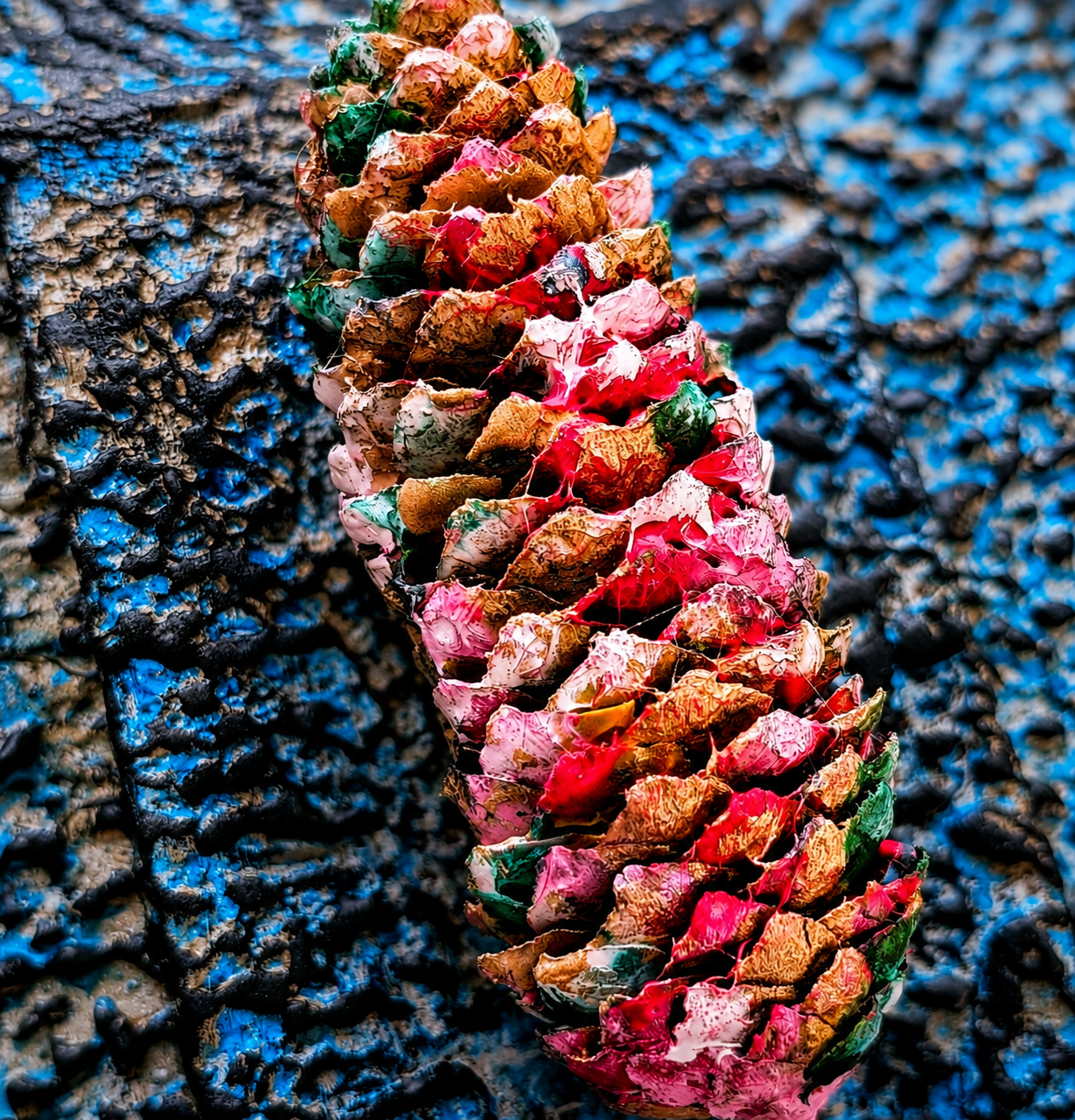 Close-up of a pine cone resting on a textured, pebbled surface.
