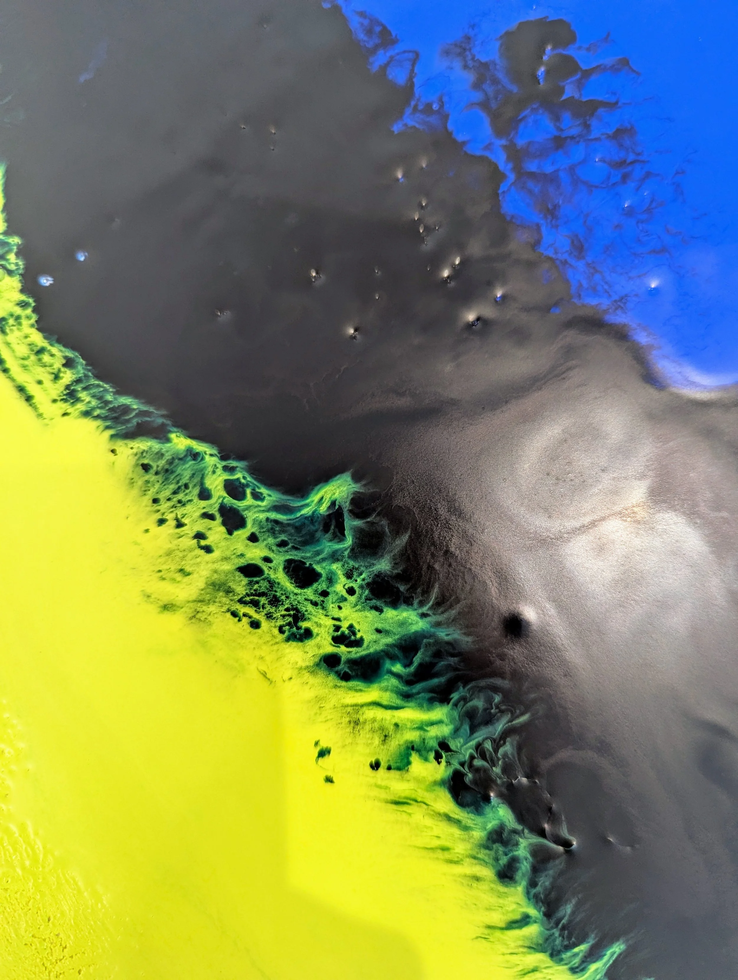 Abstract aerial view of a landscape with bright yellow, green, black, and blue colors blending together.
