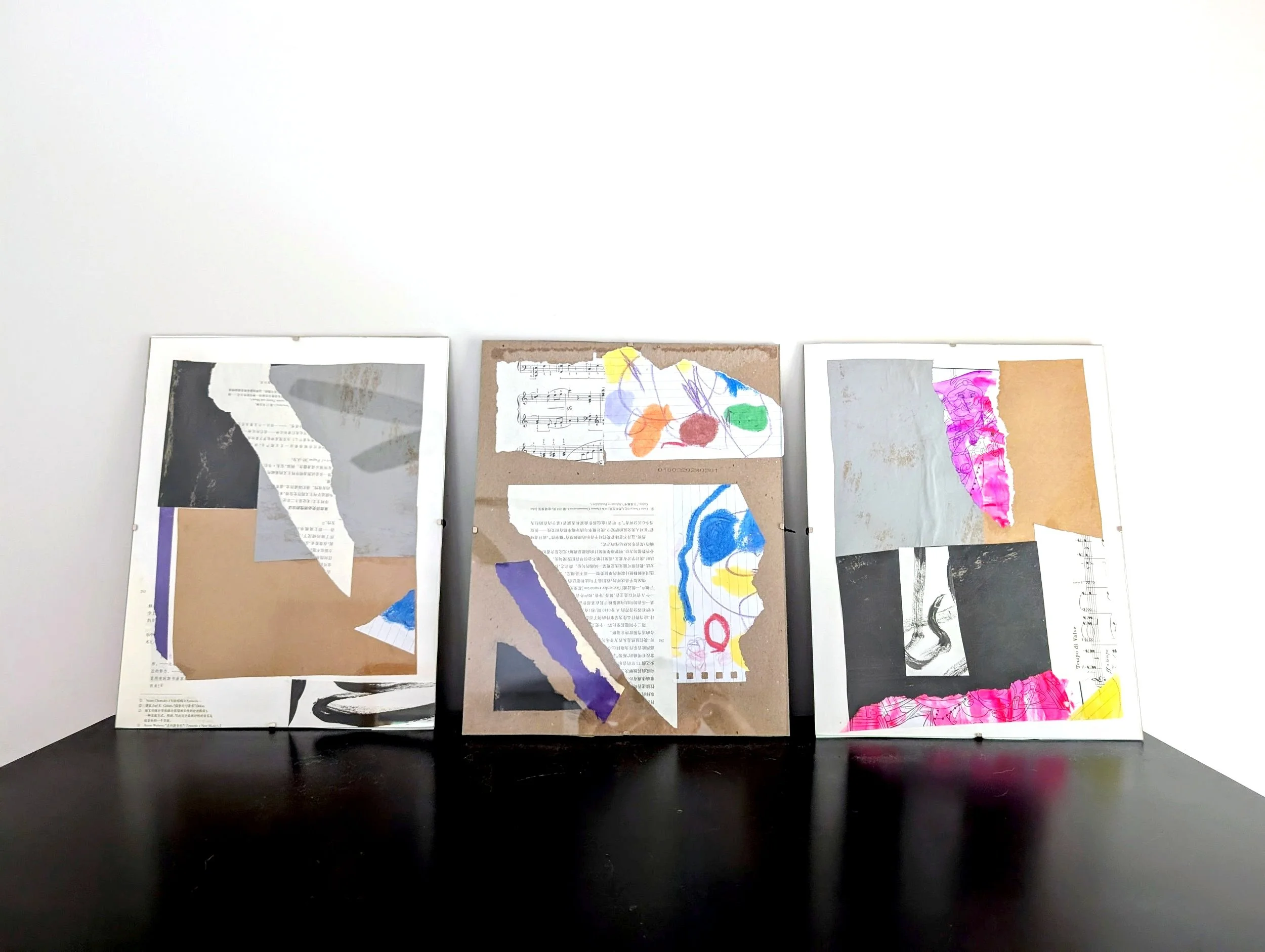Three framed abstract collages on a black surface against a white wall, featuring torn paper, drawings, and colorful shapes.