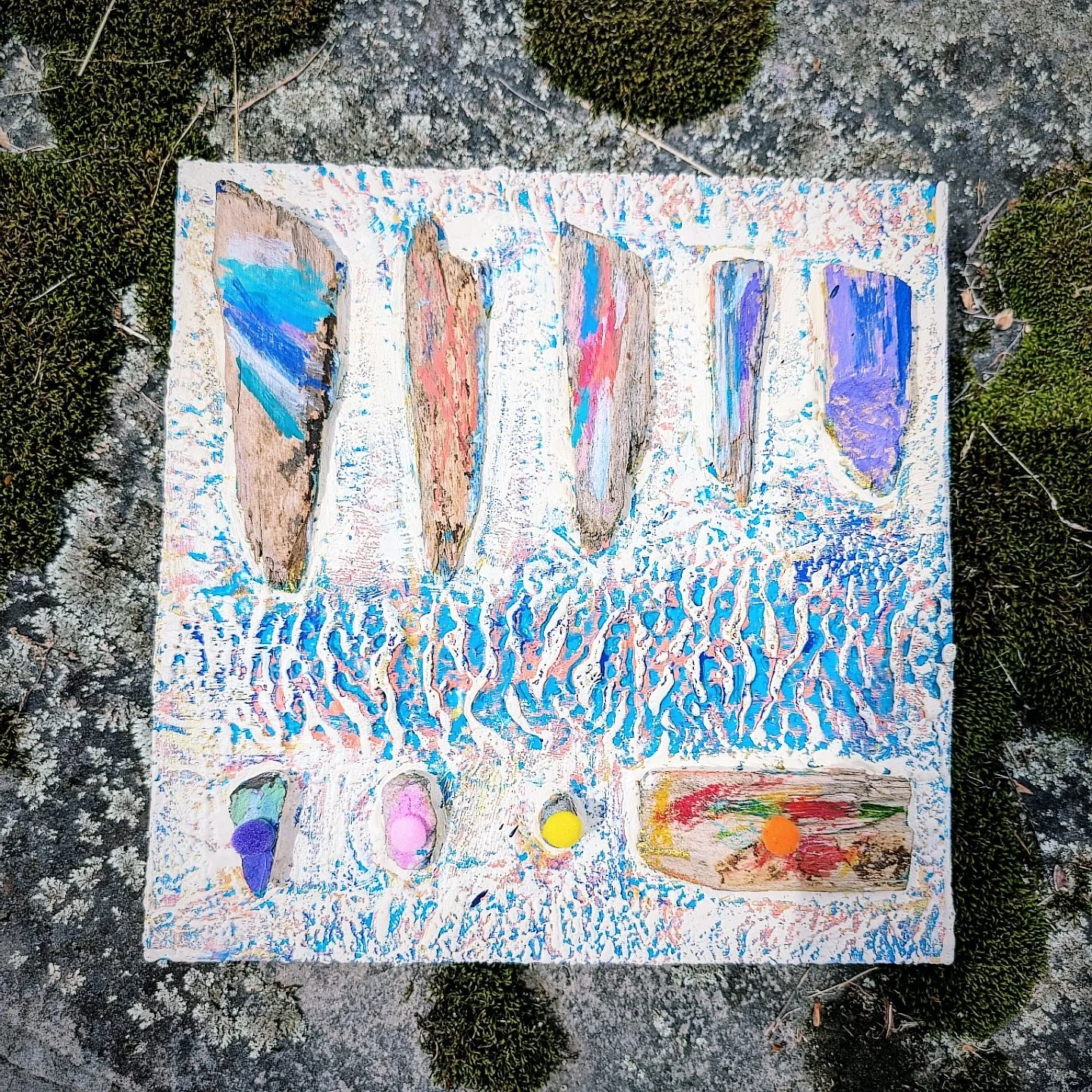 Painted rocks and pebbles on a white textured surface, with some moss around the edges.