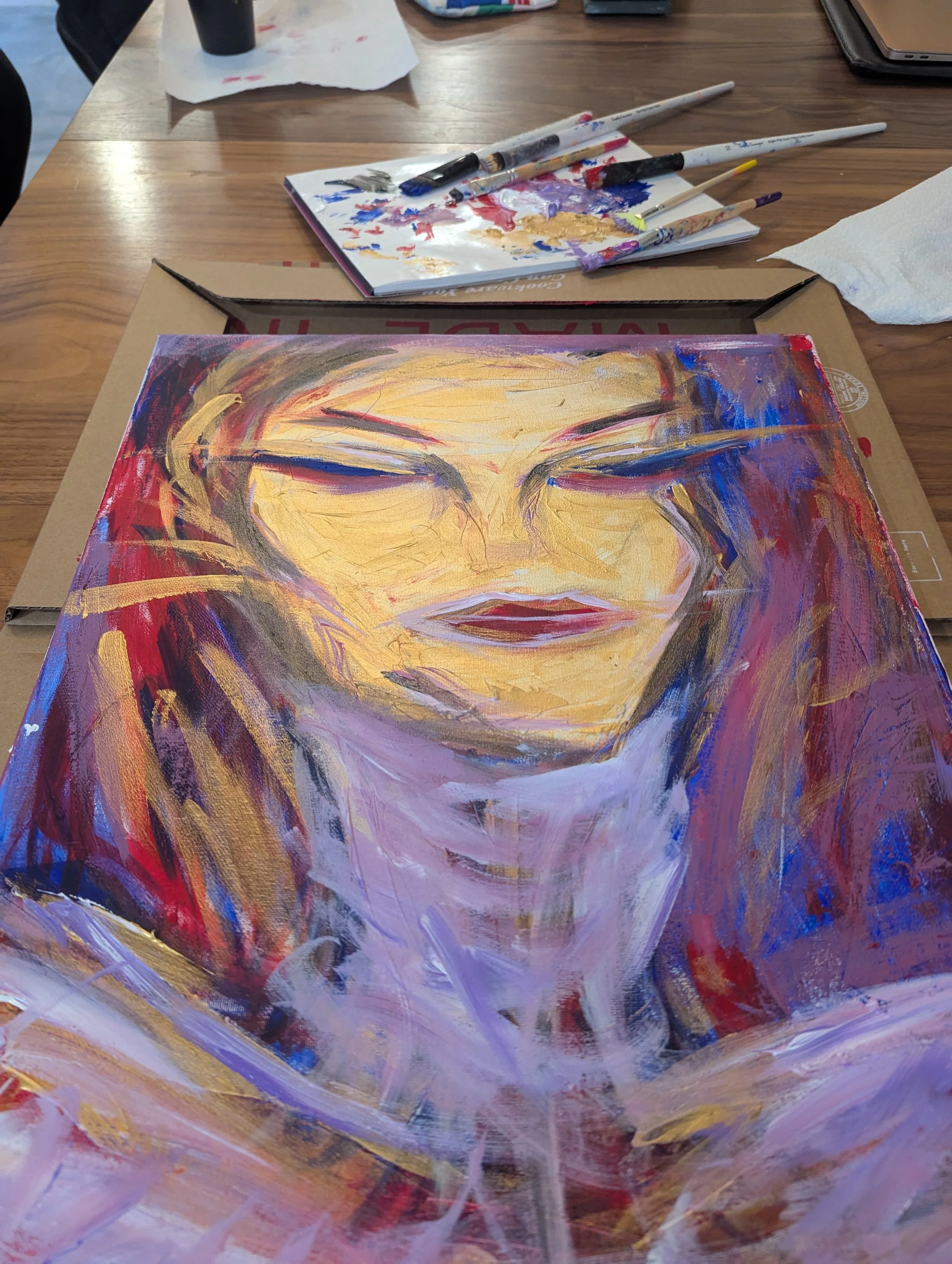A colorful abstract portrait painting of a woman with blonde hair, closed eyes, and red lips, on a canvas on a table.