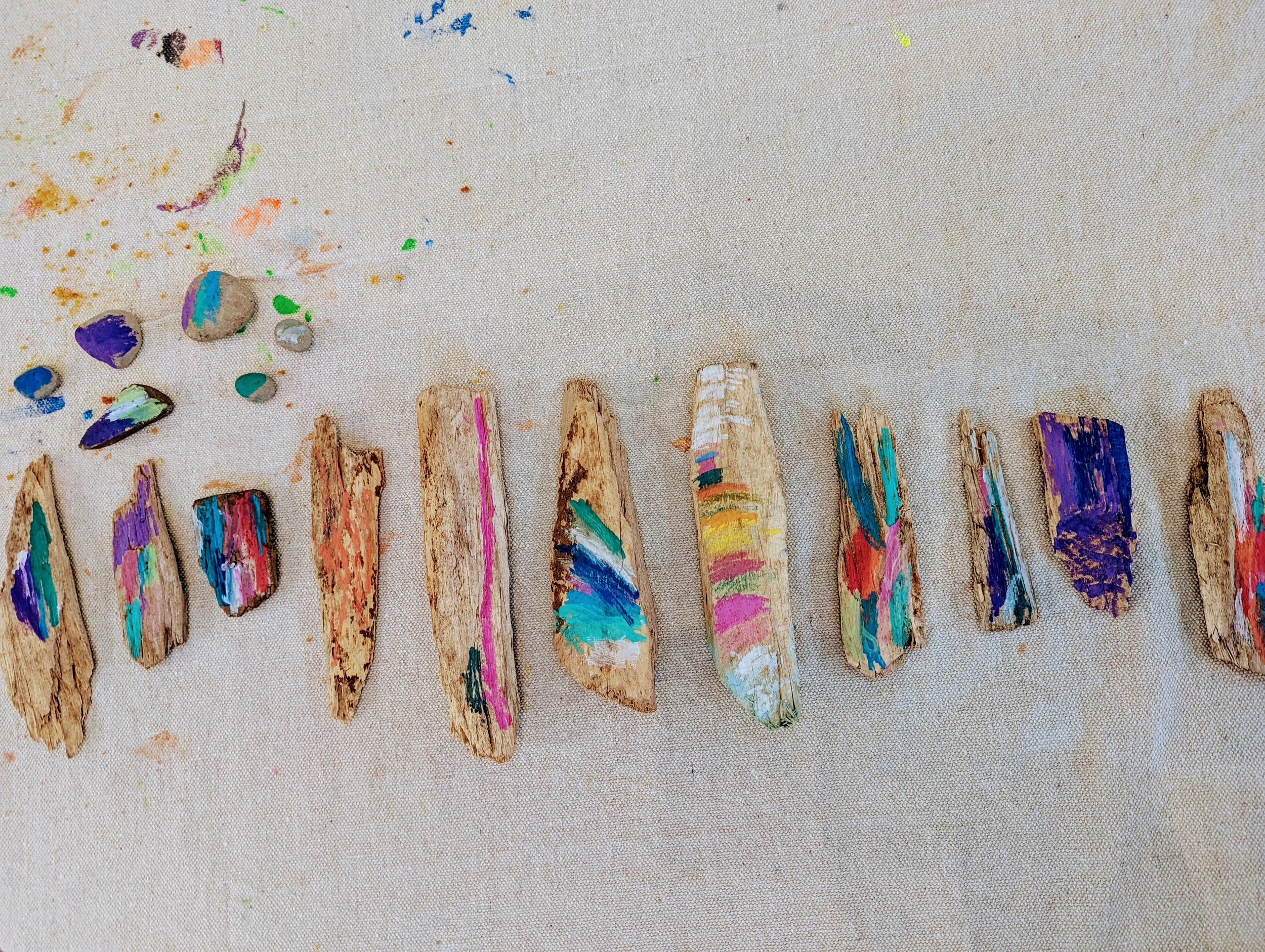 Colorful painted rocks placed on a light fabric surface with scattered paint and small stones nearby.