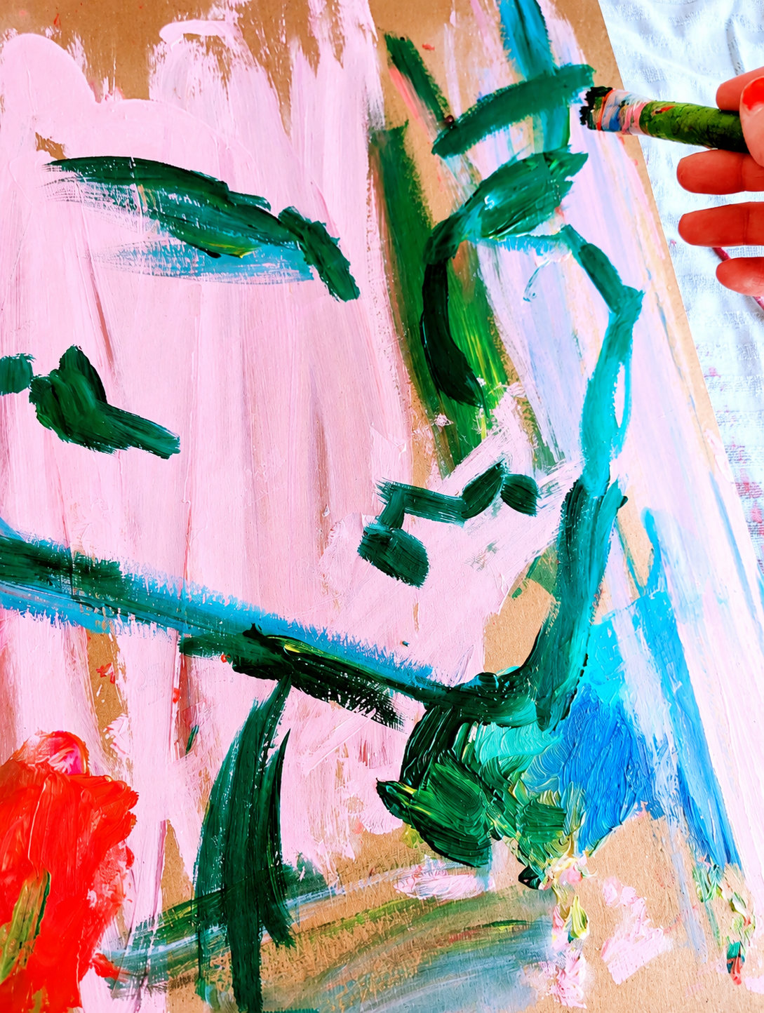 Child's vibrant, abstract watercolor painting with prominent pink background, green strokes resembling a plant or tree, and accents of red, blue, and yellow on textured paper.