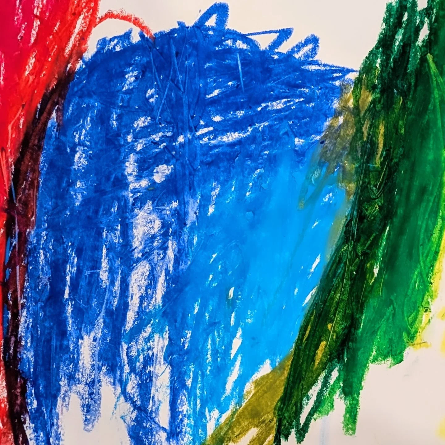 Colorful crayon drawing on paper with a large blue shape in the center, surrounded by red, green, and yellow strokes.