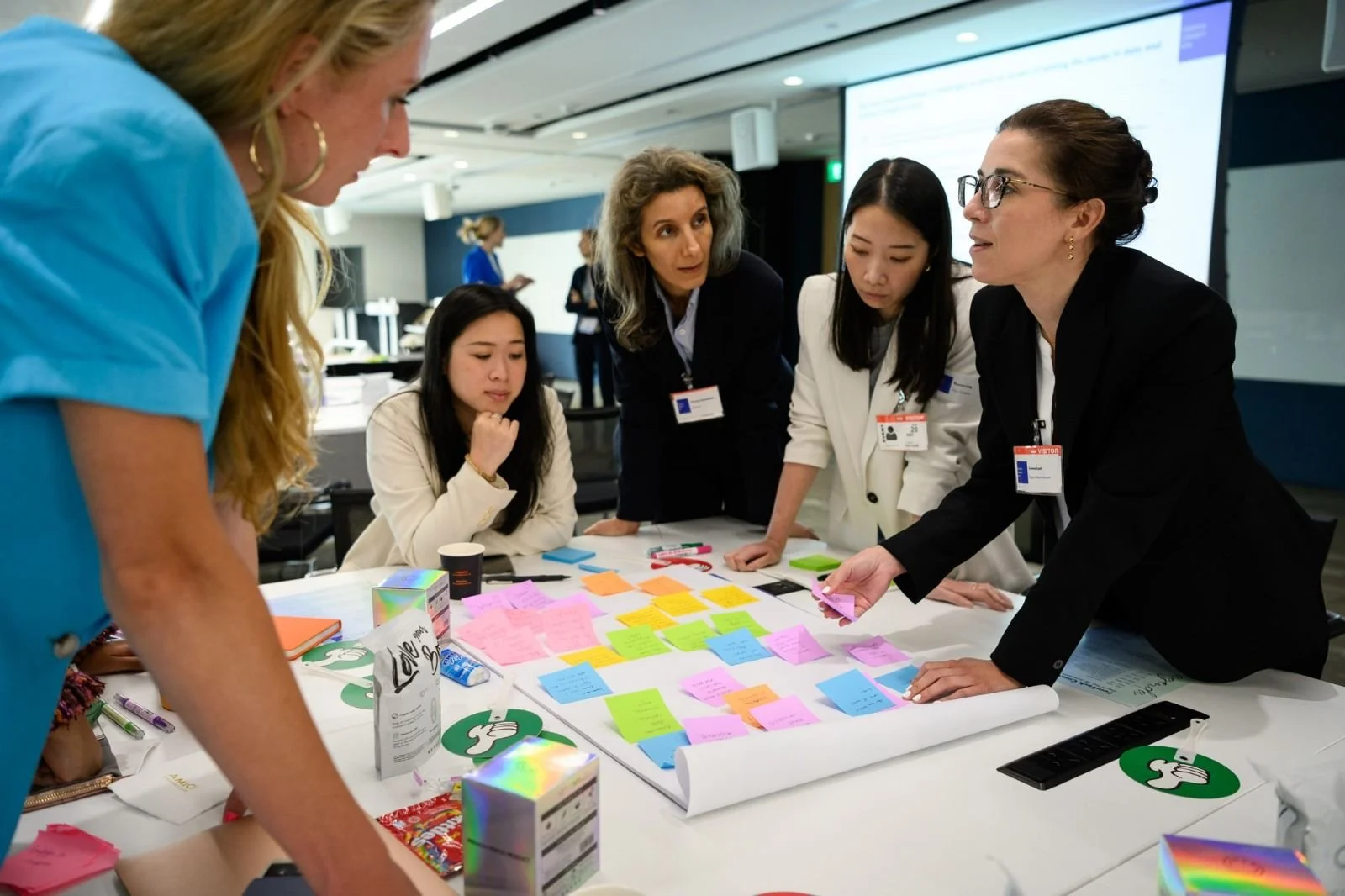 Group of women working together at a table covered with colorful sticky notes and office supplies, engaged in a collaborative discussion.