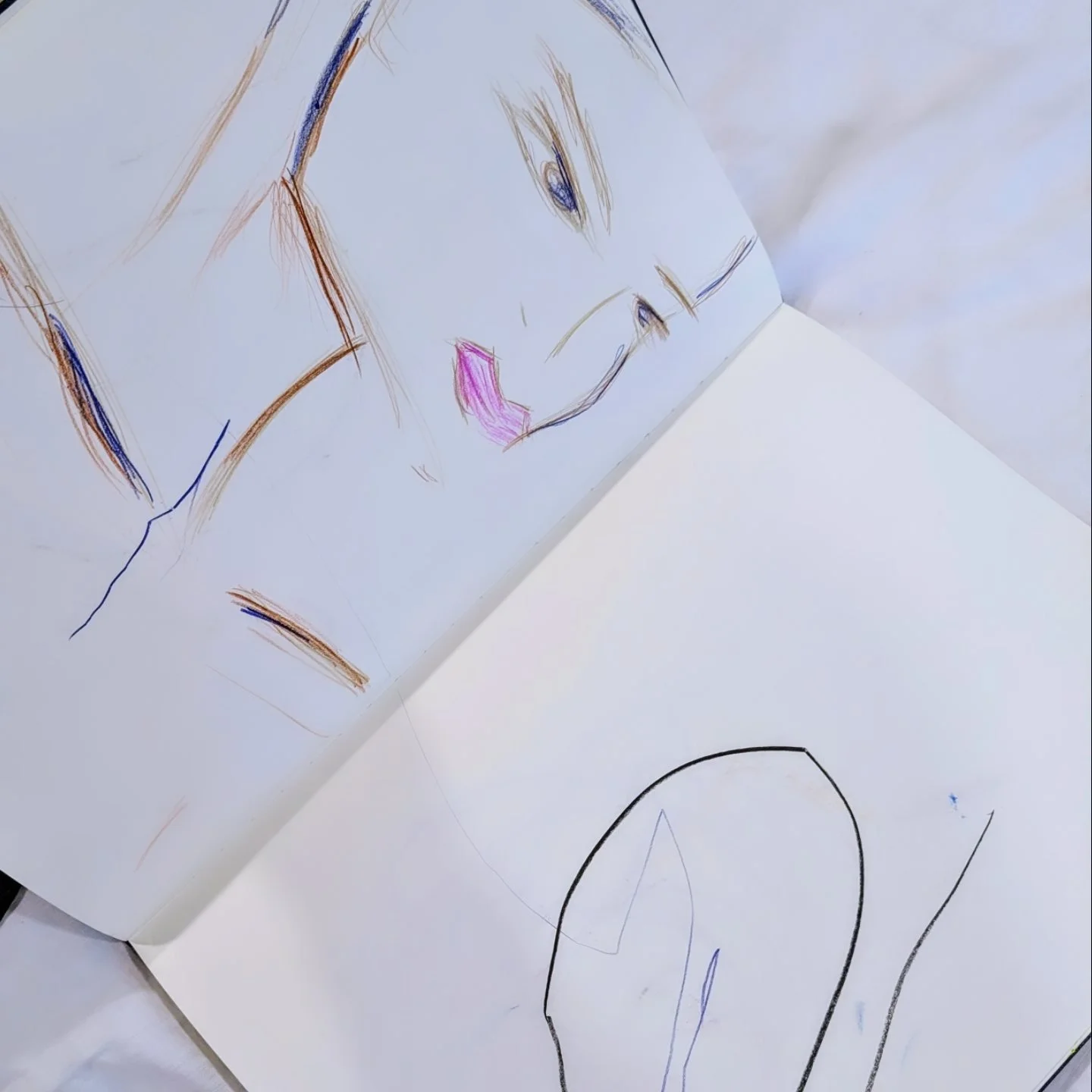 Child's drawing of a face with pink lips, blue eyes, and light brown hair, along with a simple outline of a shape on the opposite page.